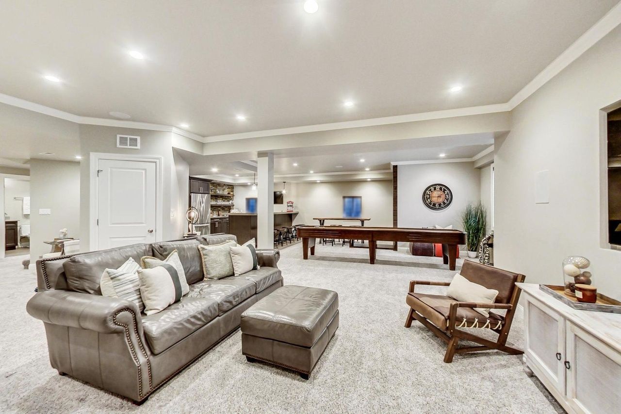 A living room with a couch , chair , ottoman and pool table.