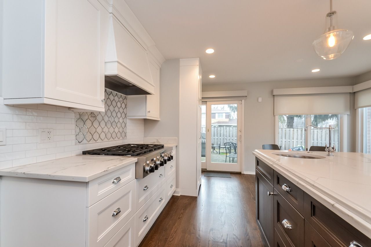 A kitchen with white cabinets , a stove , a sink , and a large island.