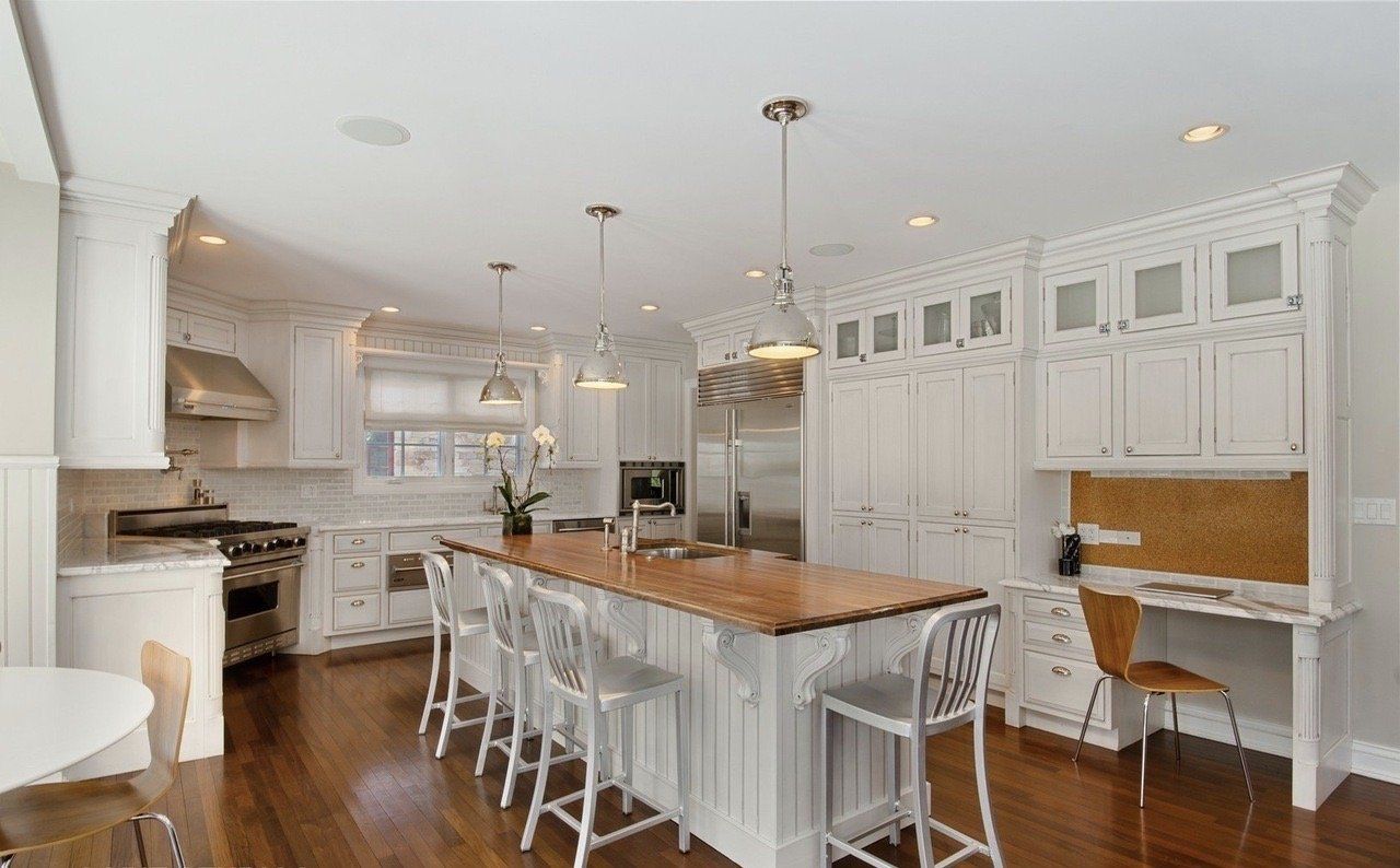 A kitchen with white cabinets , stainless steel appliances , hardwood floors and a large island.