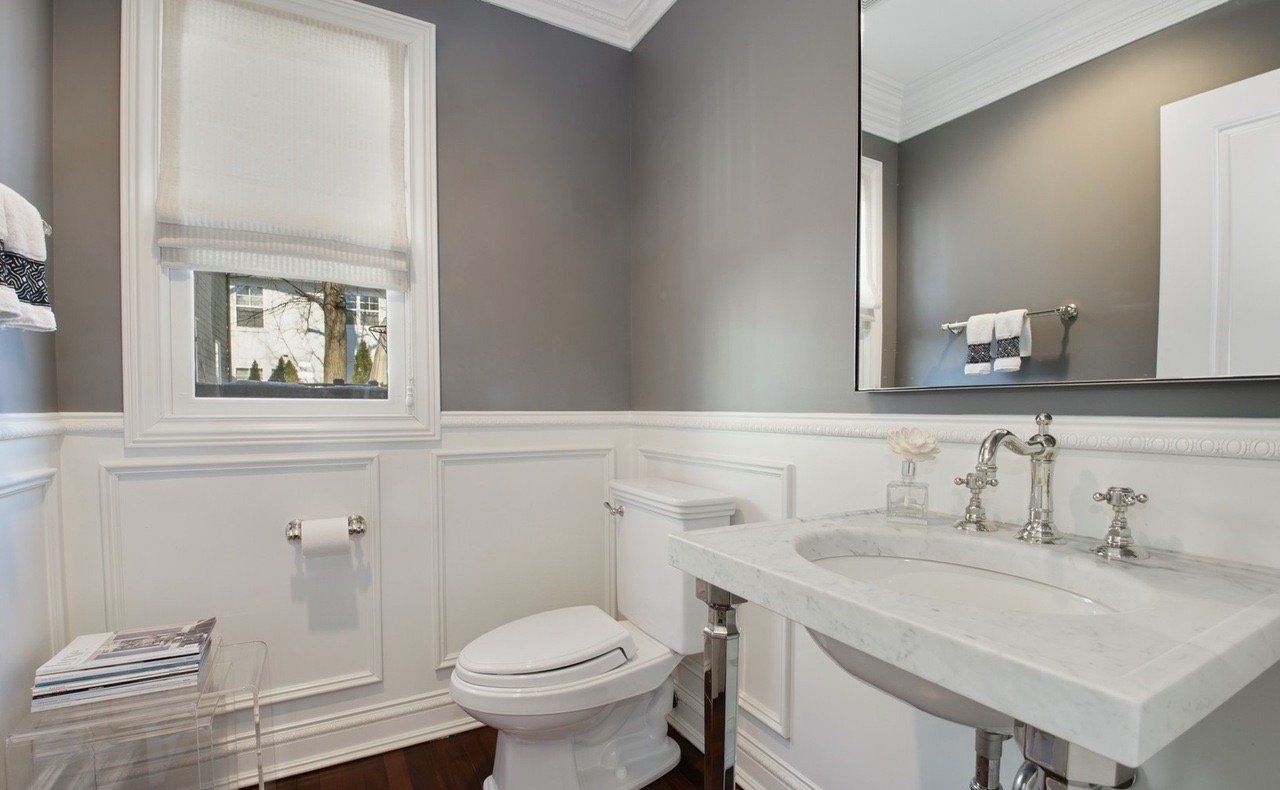 A bathroom with a toilet , sink , mirror and window.