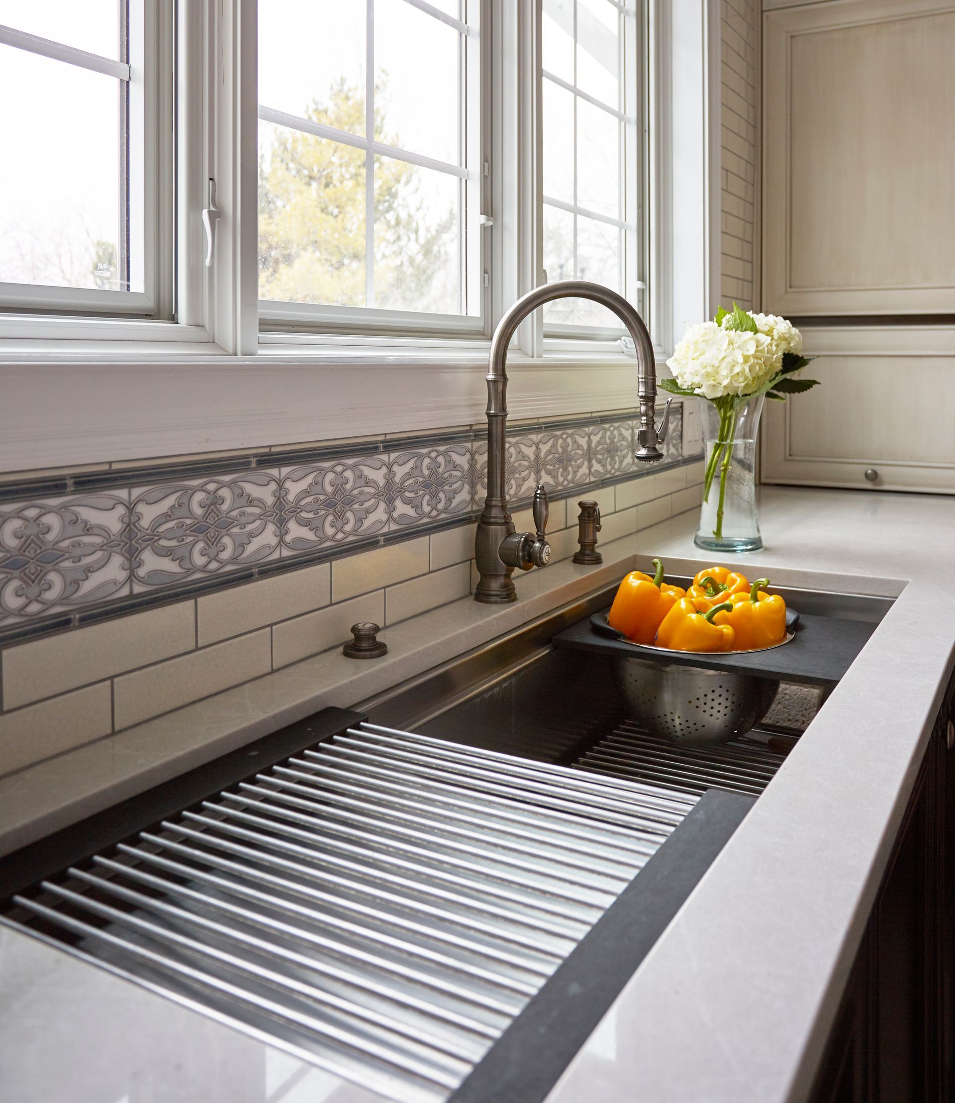 A kitchen sink with a bowl of peppers and a vase of flowers on the counter.
