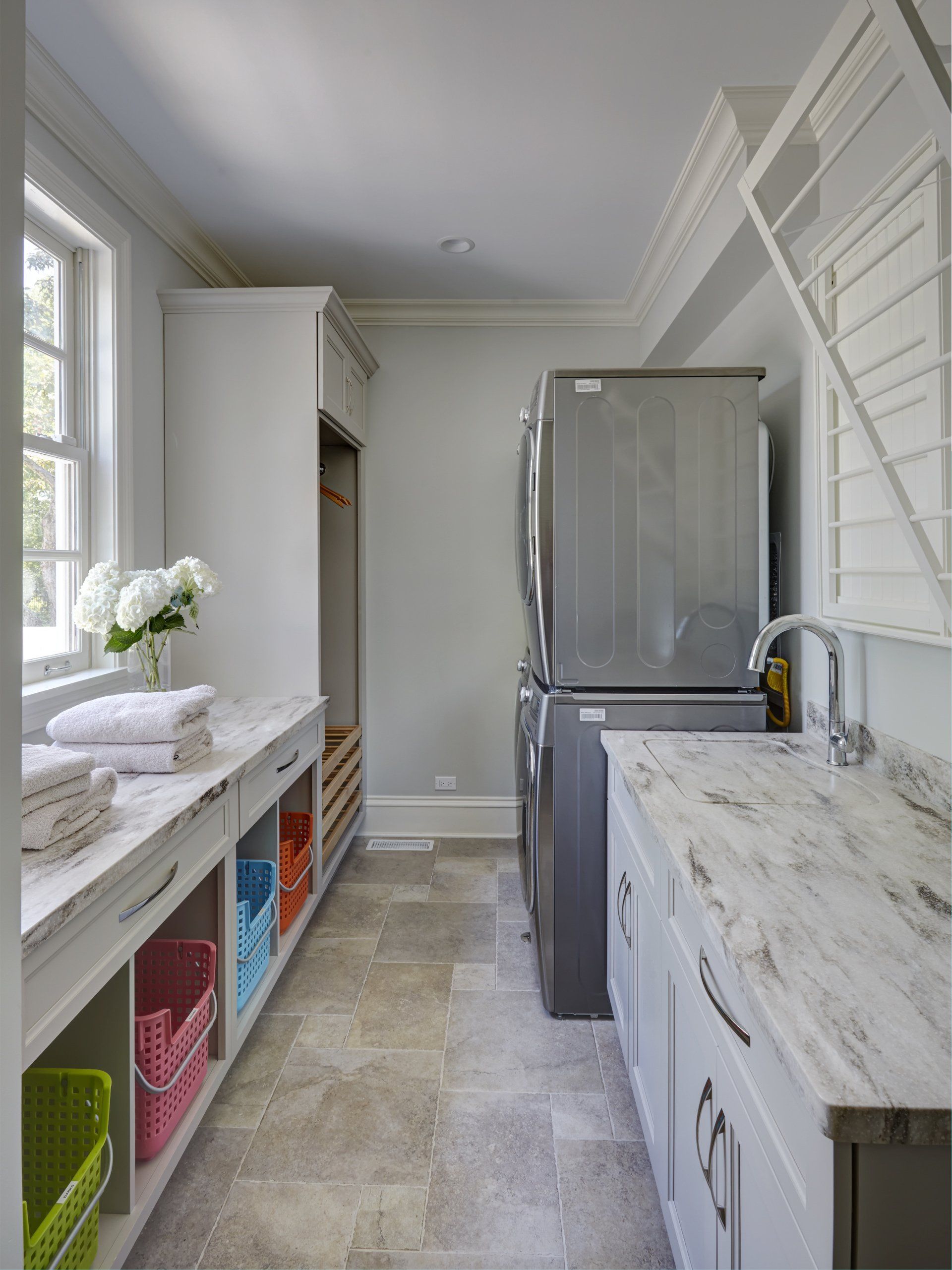 A laundry room with white cabinets and marble counter tops