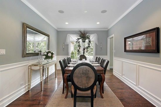 A dining room with a long table and chairs and a mirror on the wall.
