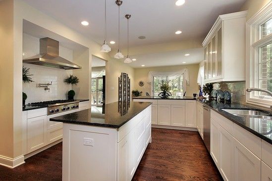 A kitchen with white cabinets , black counter tops , and a large island.