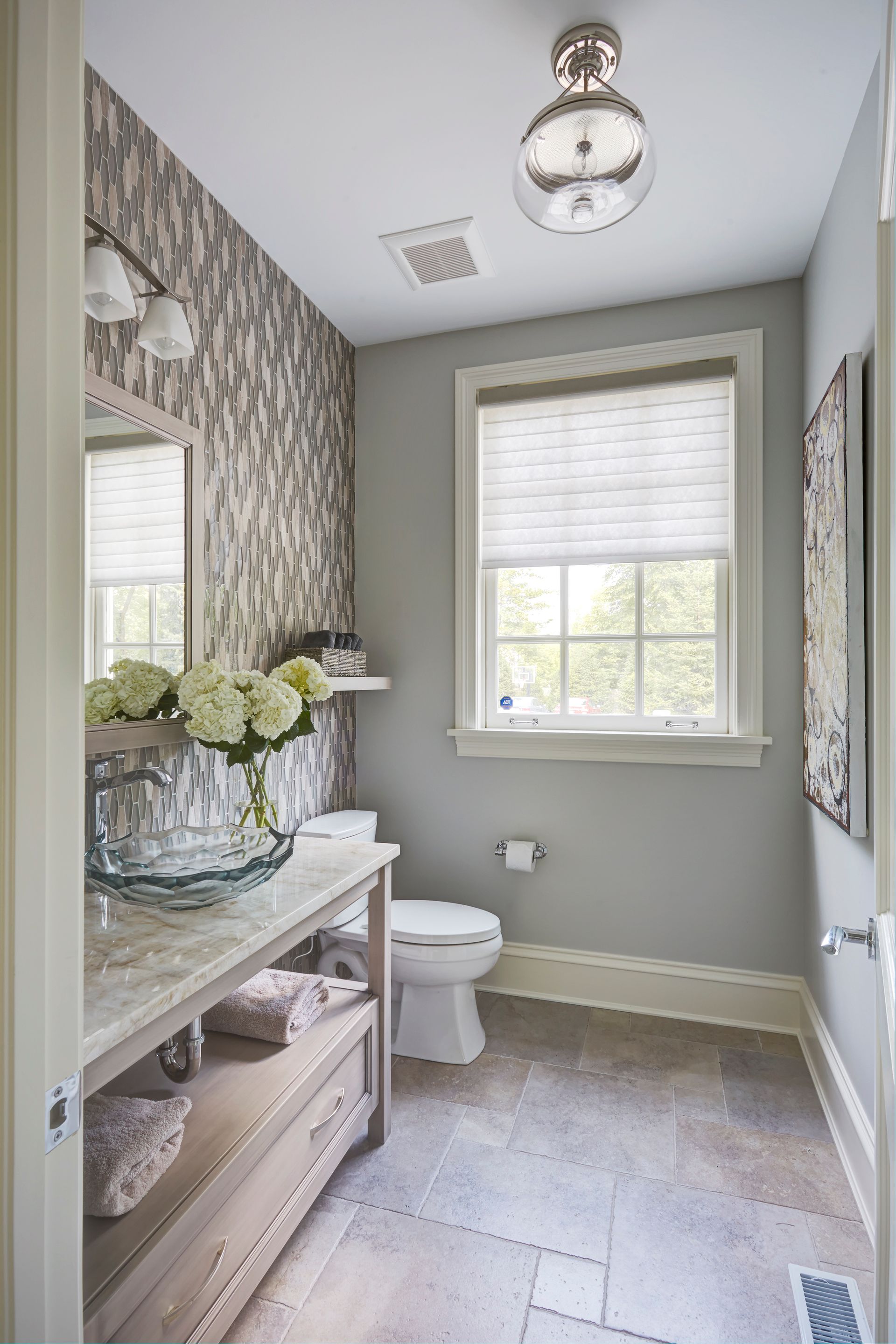 A bathroom with a toilet , sink , mirror and window.