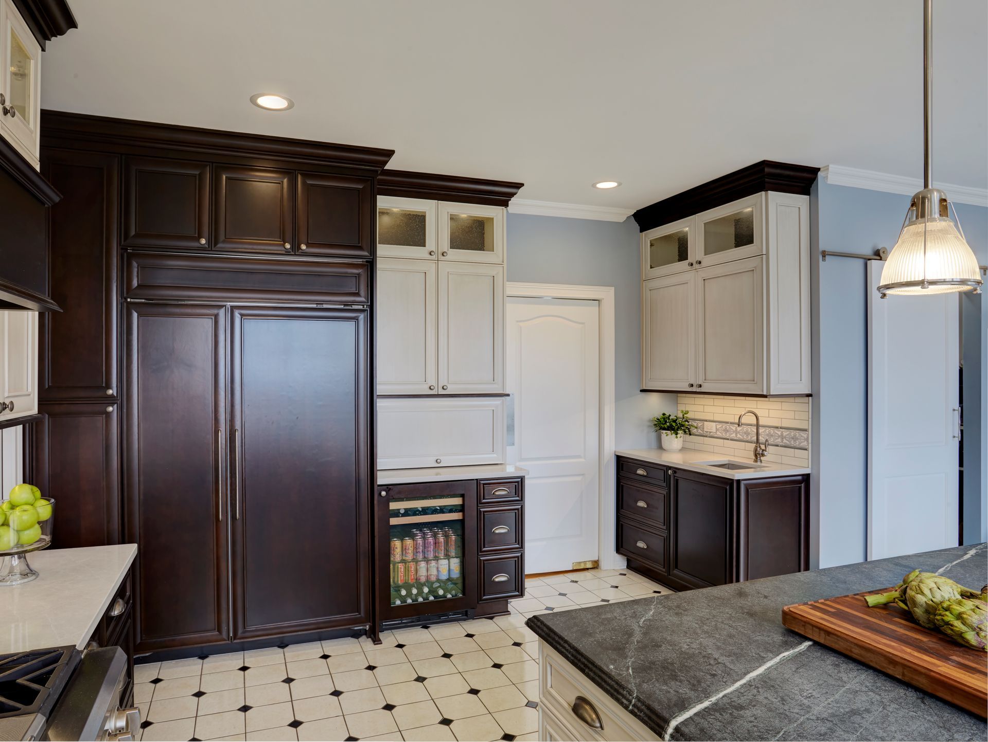 A kitchen with dark cabinets and white cabinets and a cutting board on the counter.