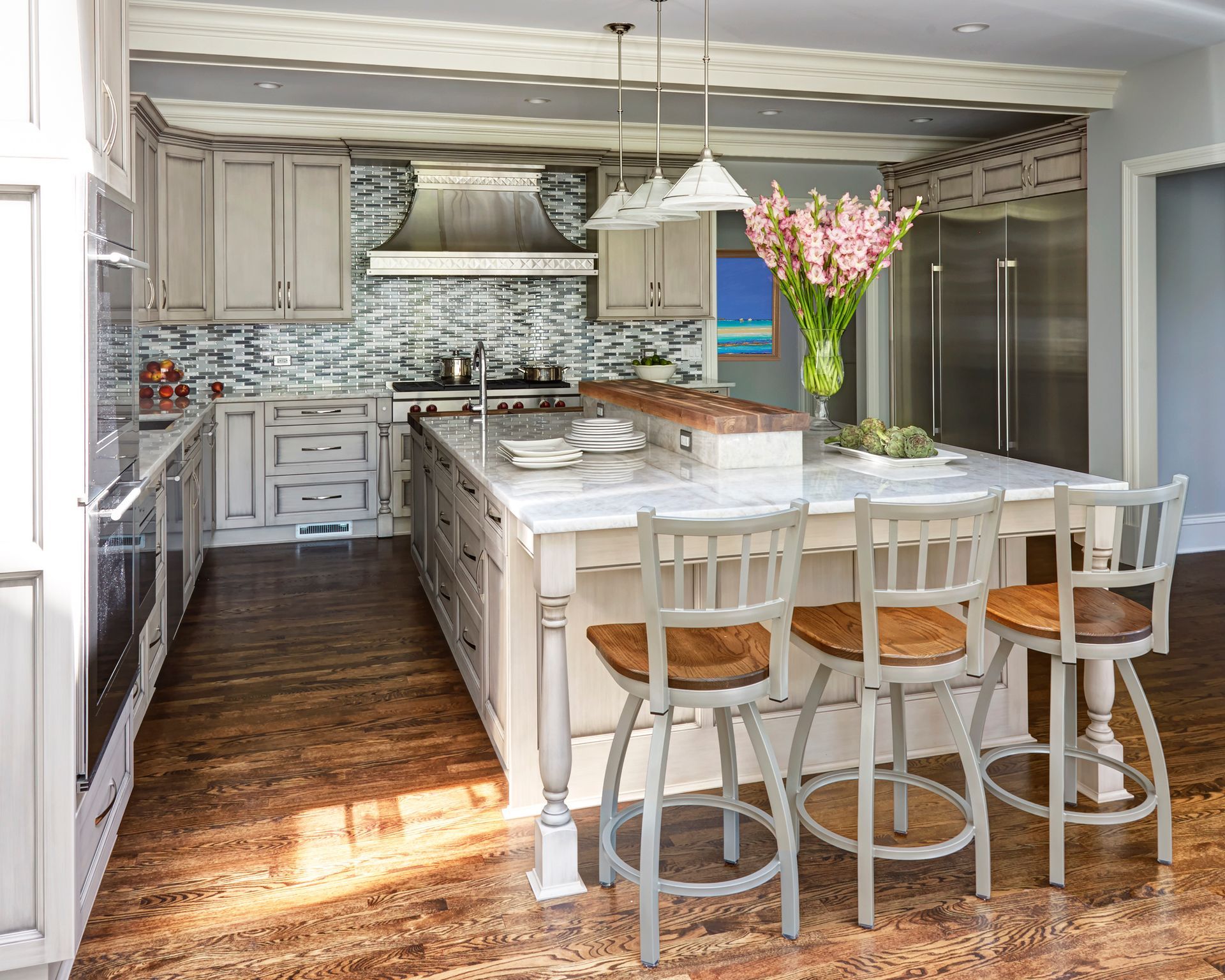 A kitchen with a large island and stools and a vase of flowers on the counter.