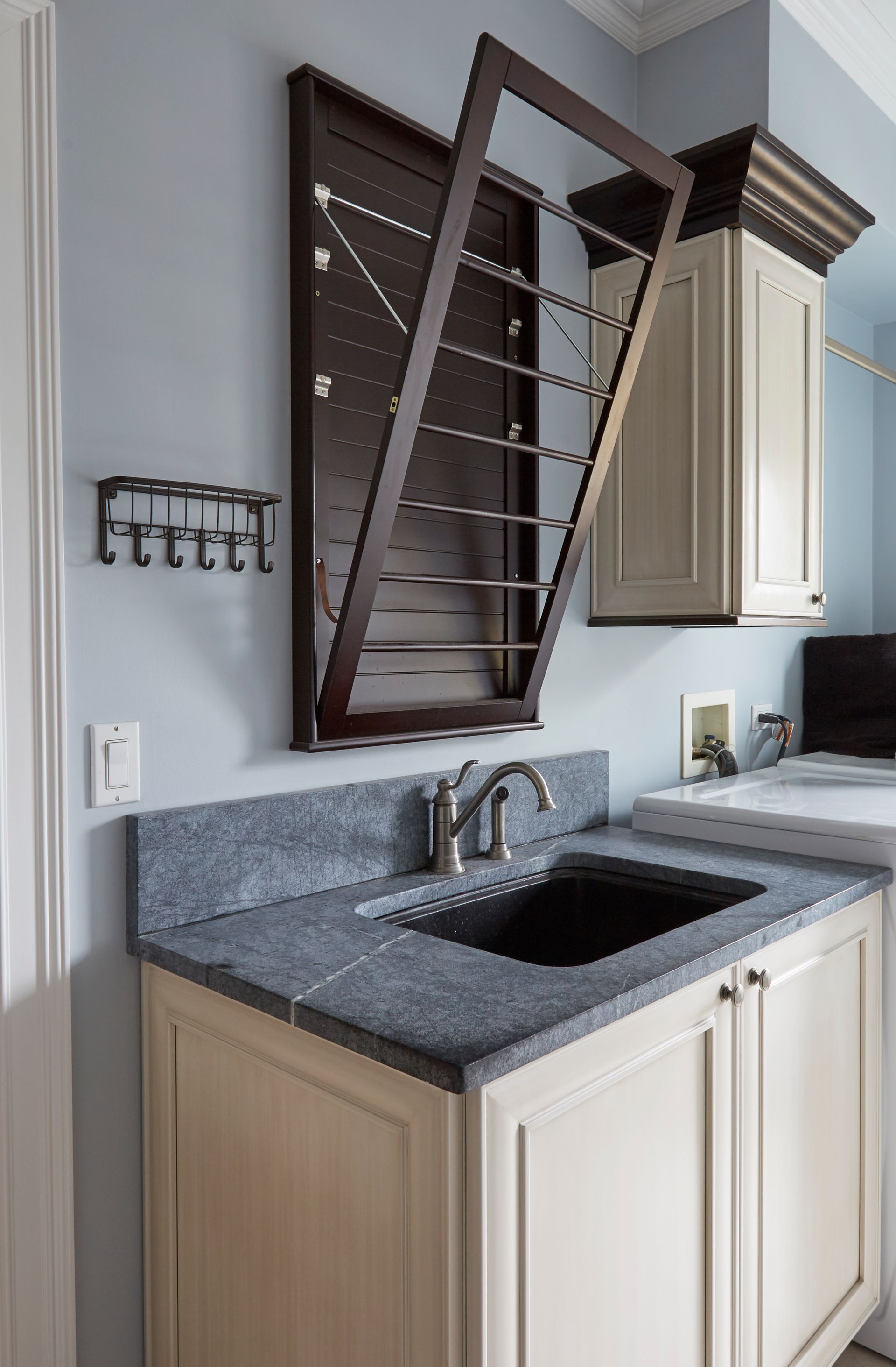 A laundry room with a sink , cabinets , and a clothes drying rack.