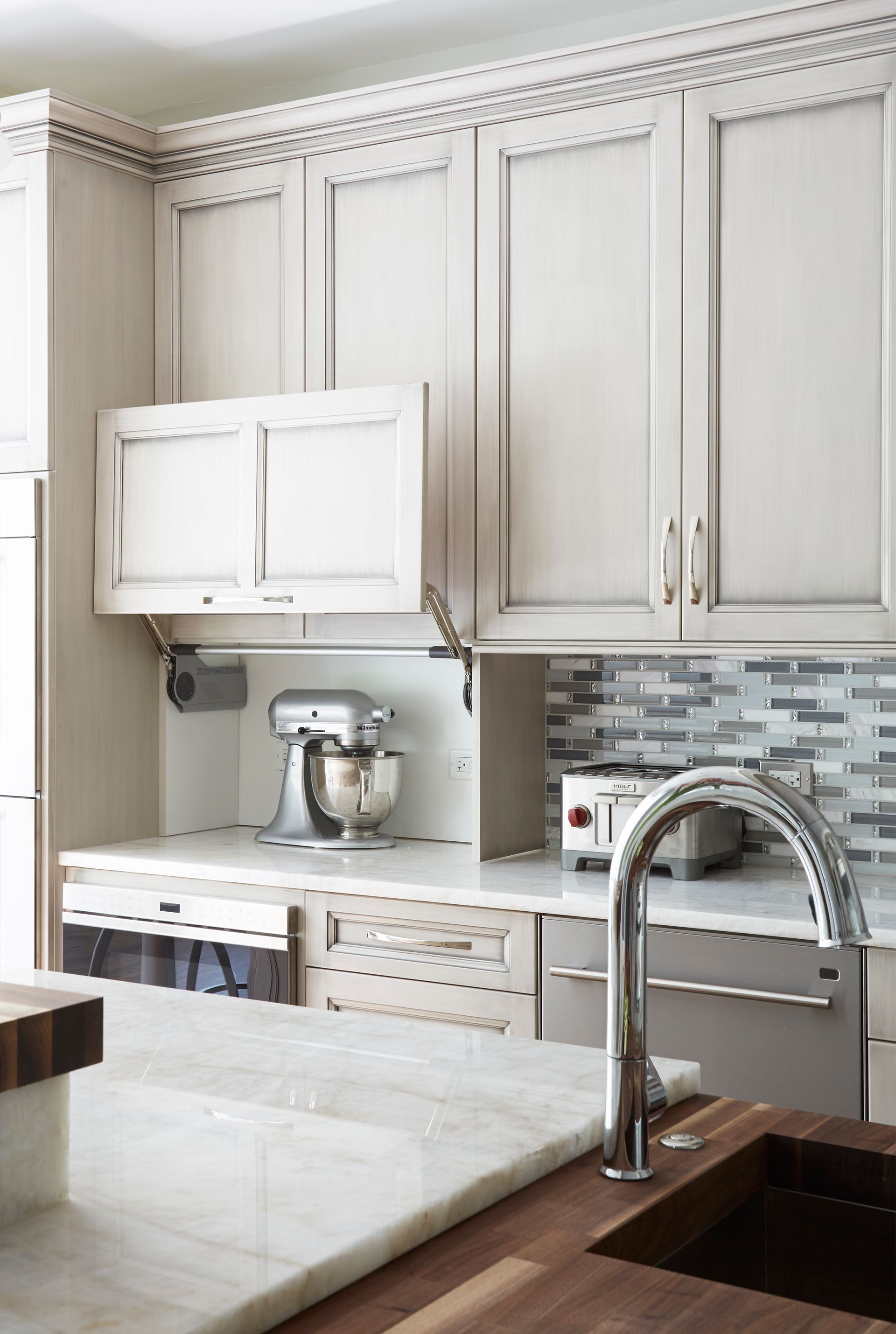 A kitchen with white cabinets , a sink , a toaster oven , and a mixer.