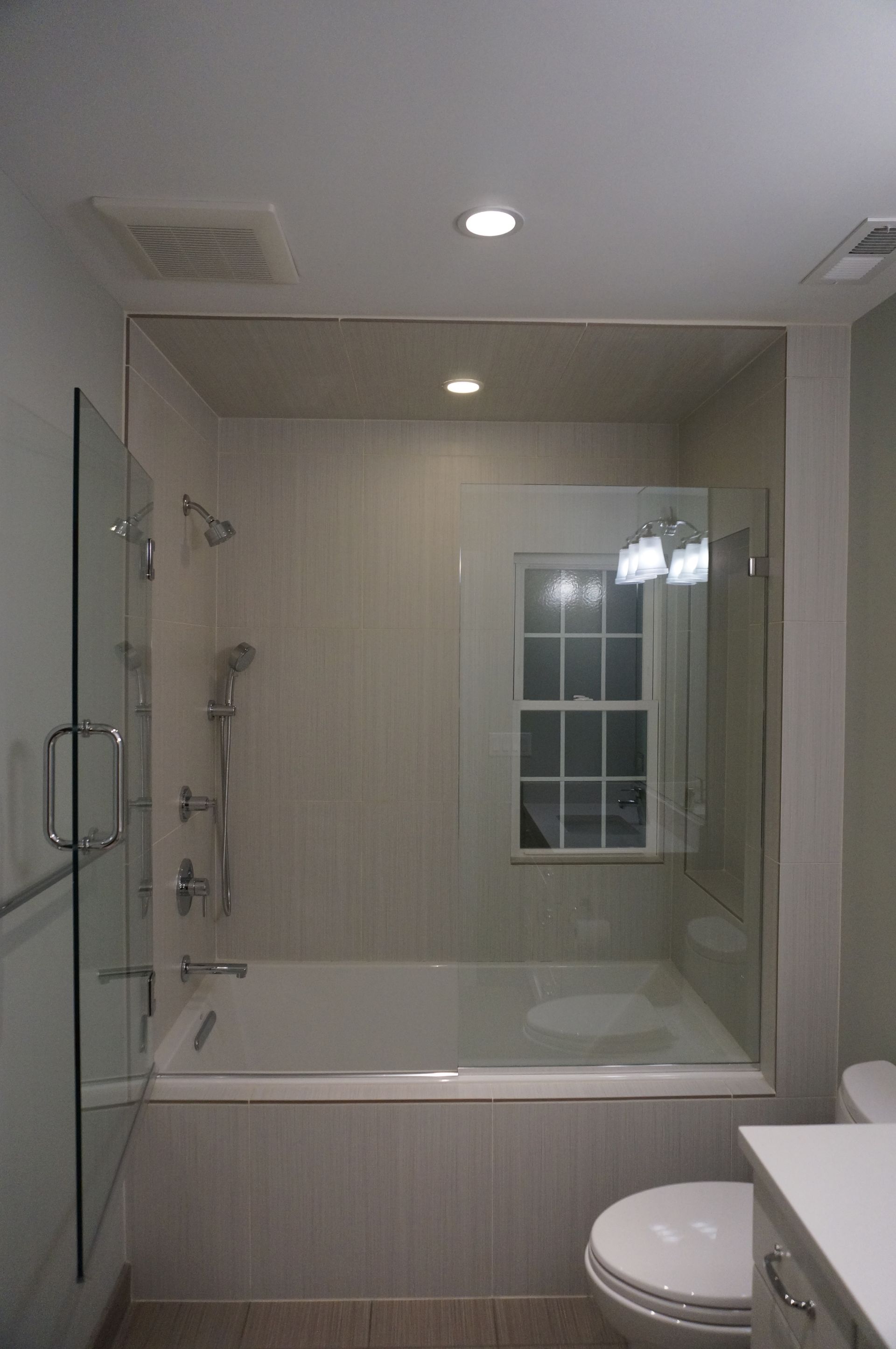 A bathroom with a tub , toilet , shower and window.