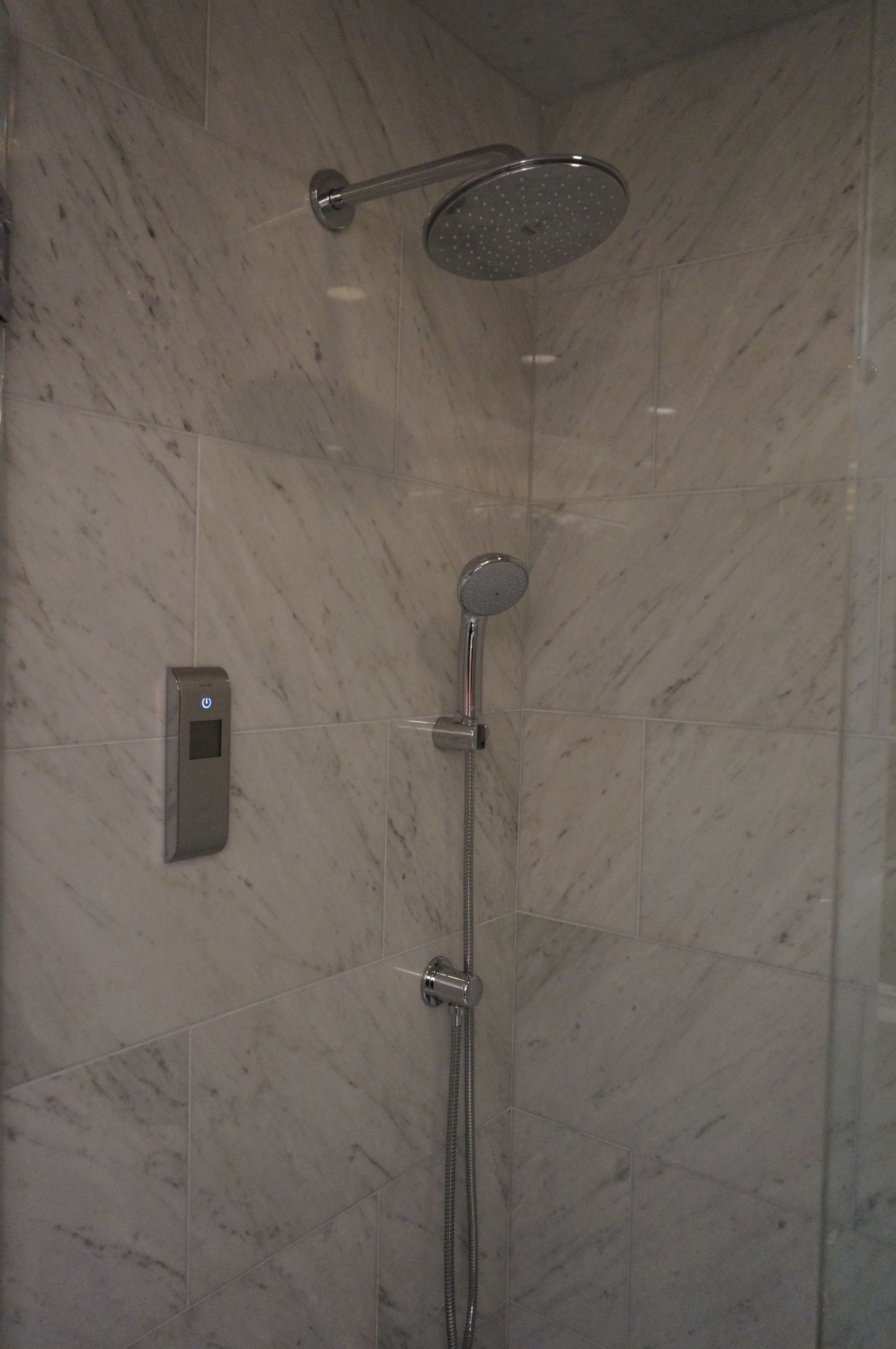 A shower head is hanging from a marble wall in a bathroom.