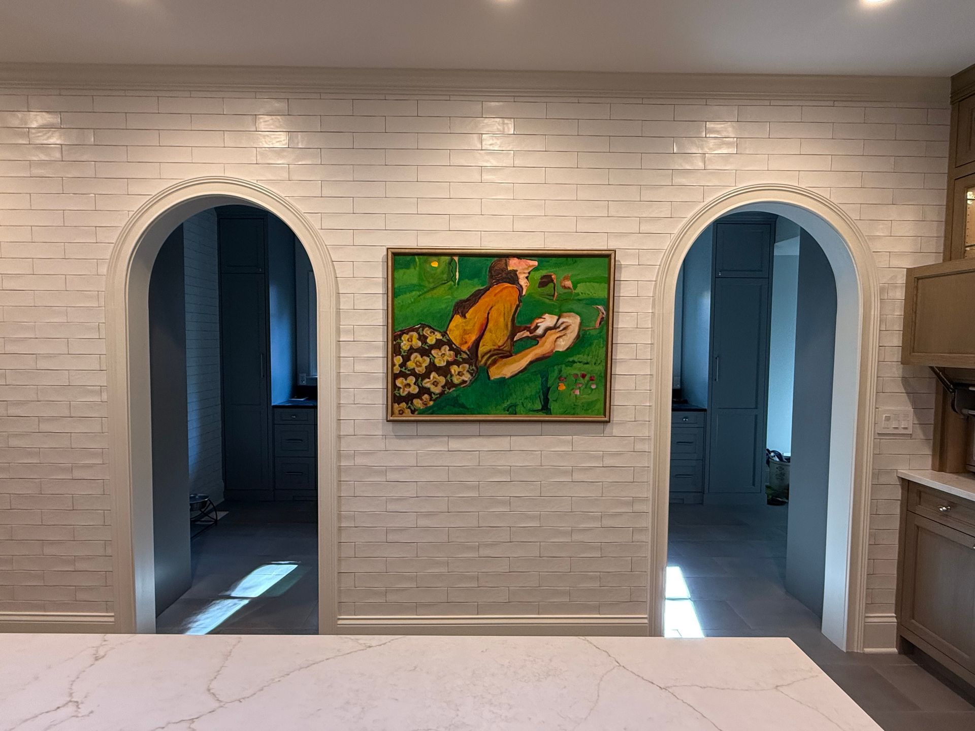 A painting is hanging on a white brick wall in a kitchen.