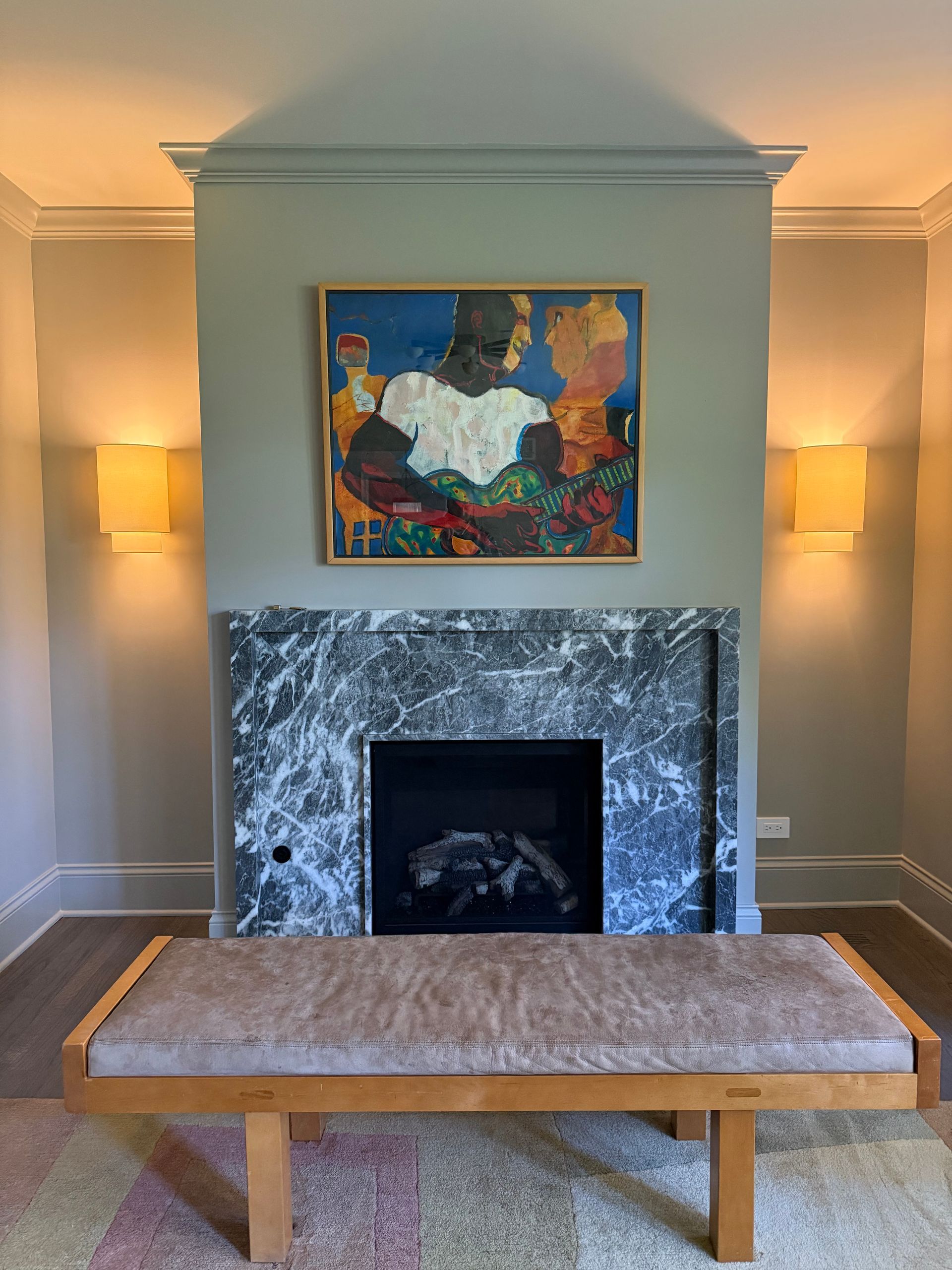 A fireplace with a painting above it and a bench in front of it.