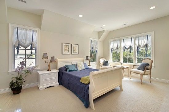 A bedroom with a sleigh bed , chairs , nightstands and two windows.