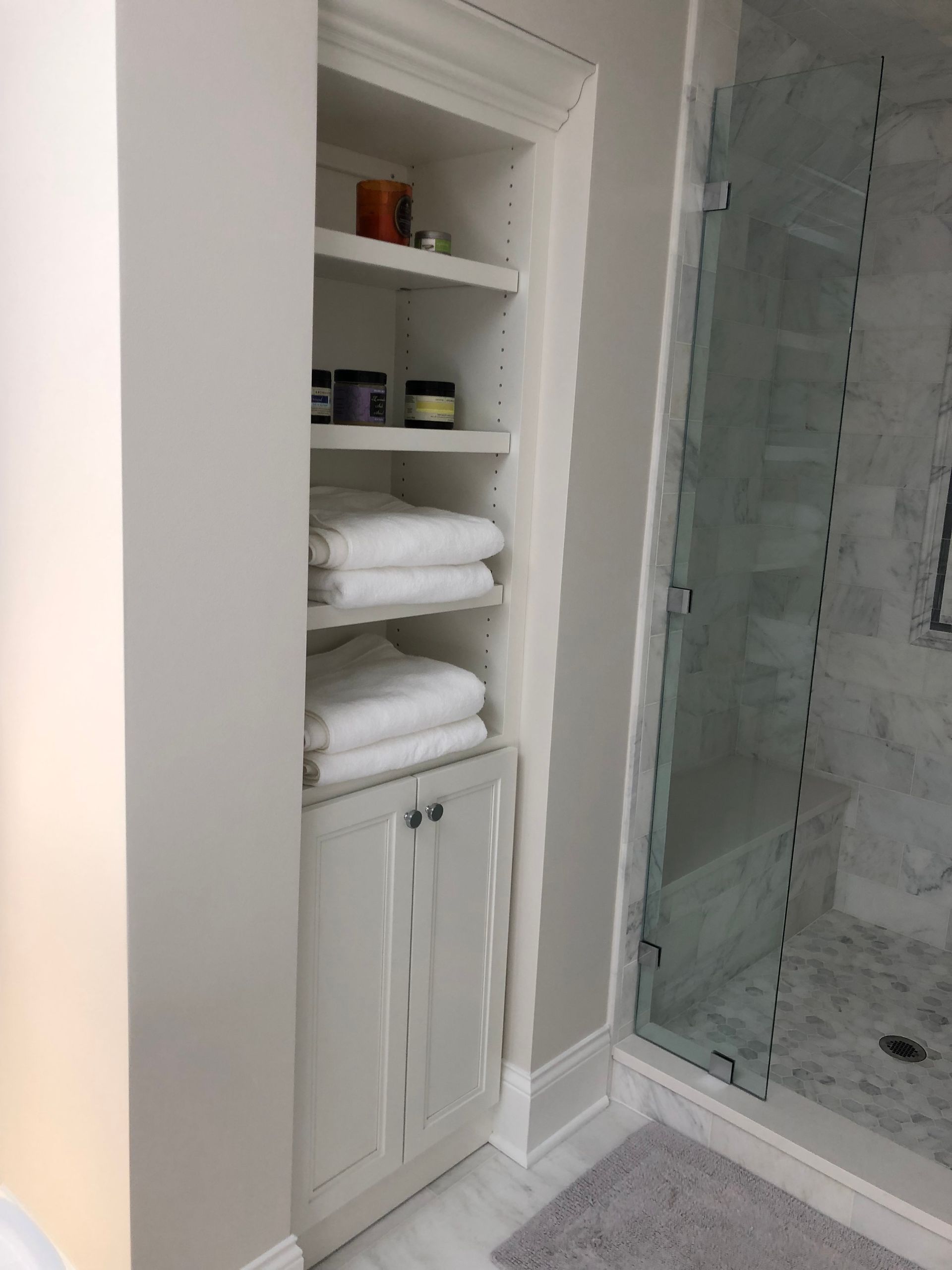 A bathroom with a shower and a shelf with towels on it