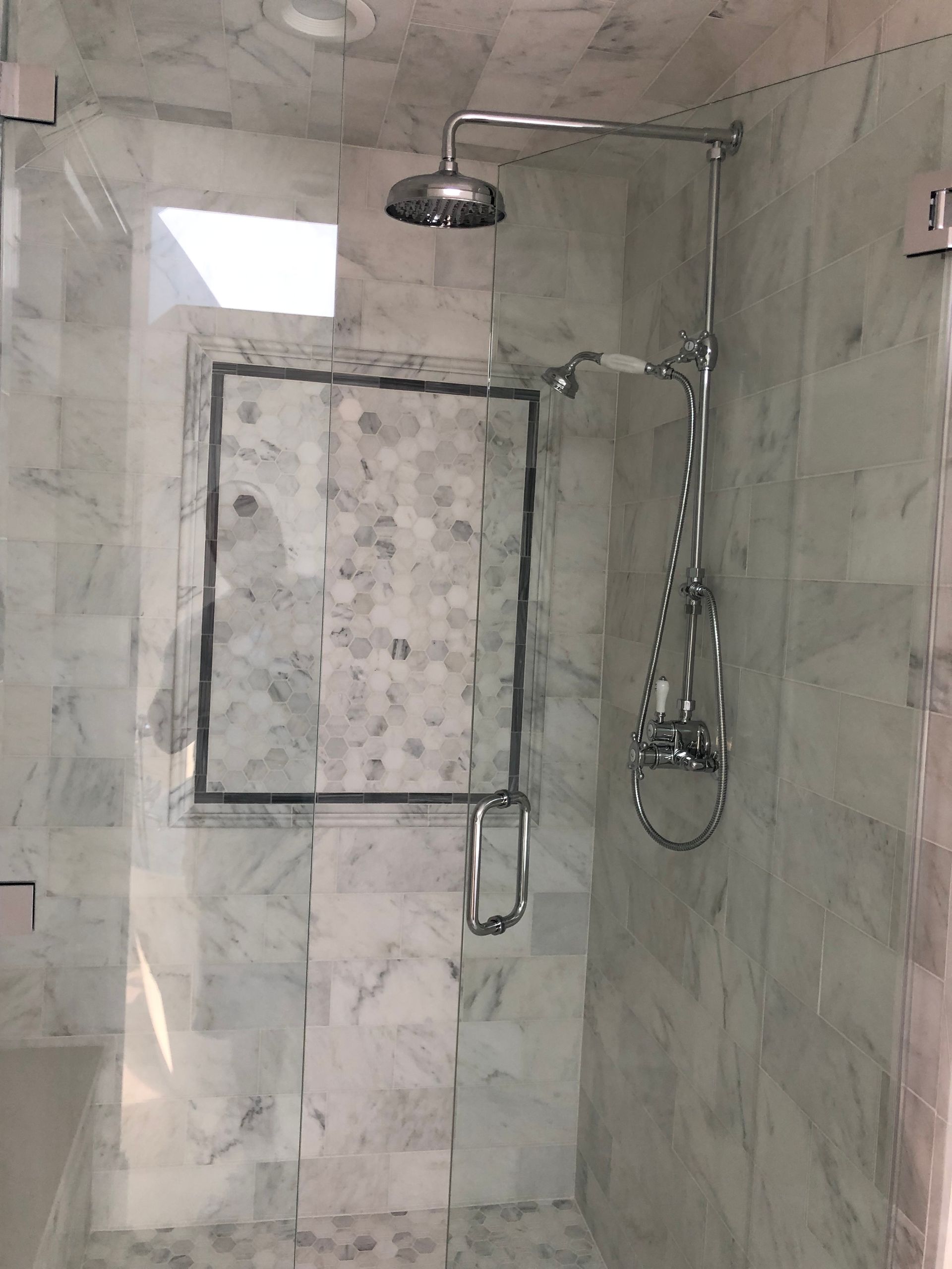 A shower with a marble wall and a shower head.