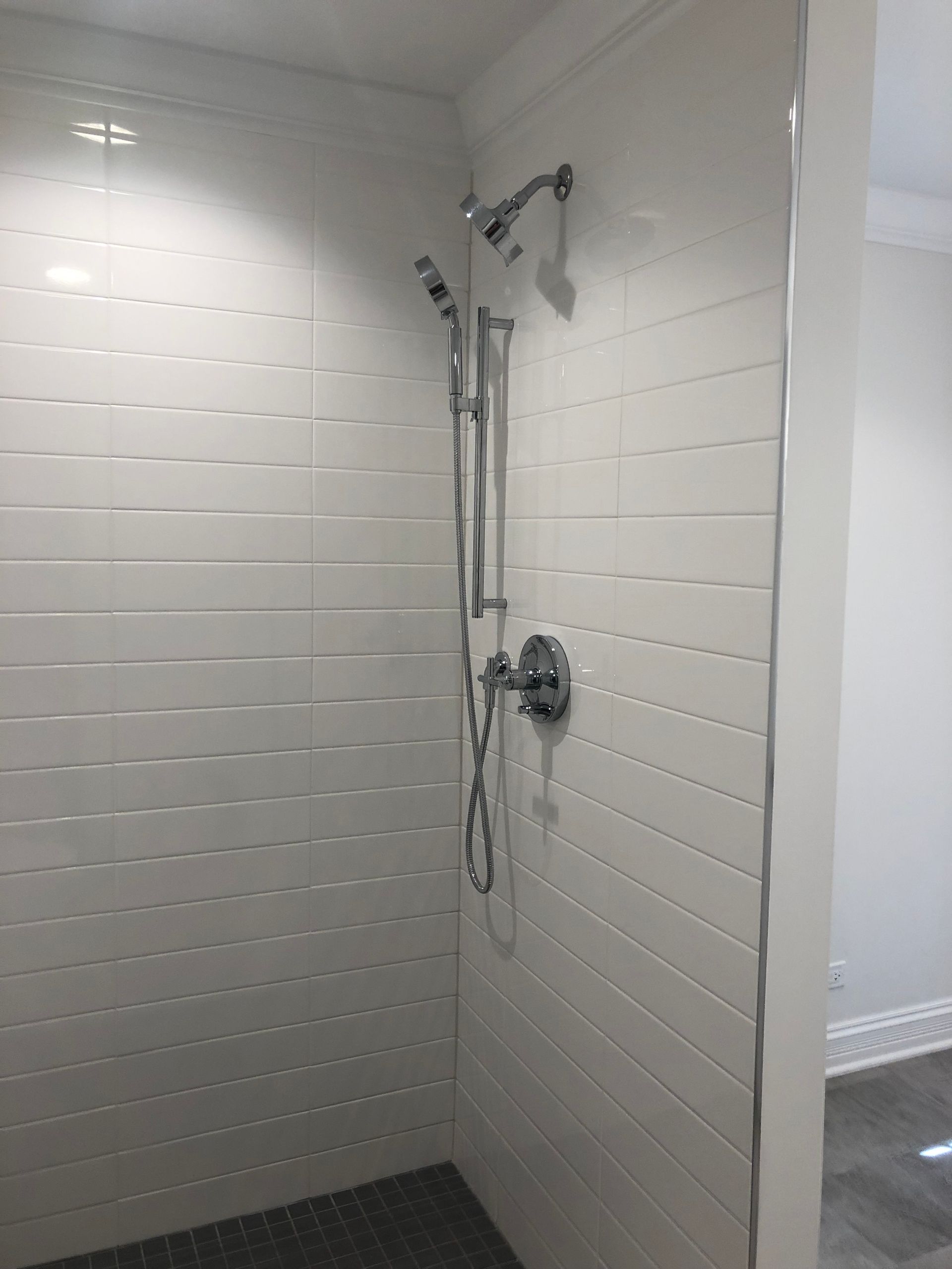 A shower with white tiles and a chrome shower head.