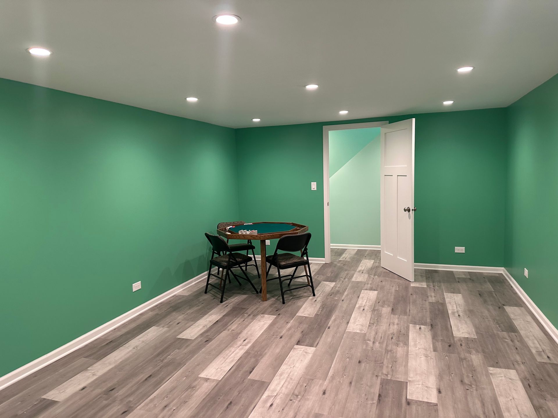 A basement with green walls and wooden floors and a table and chairs.