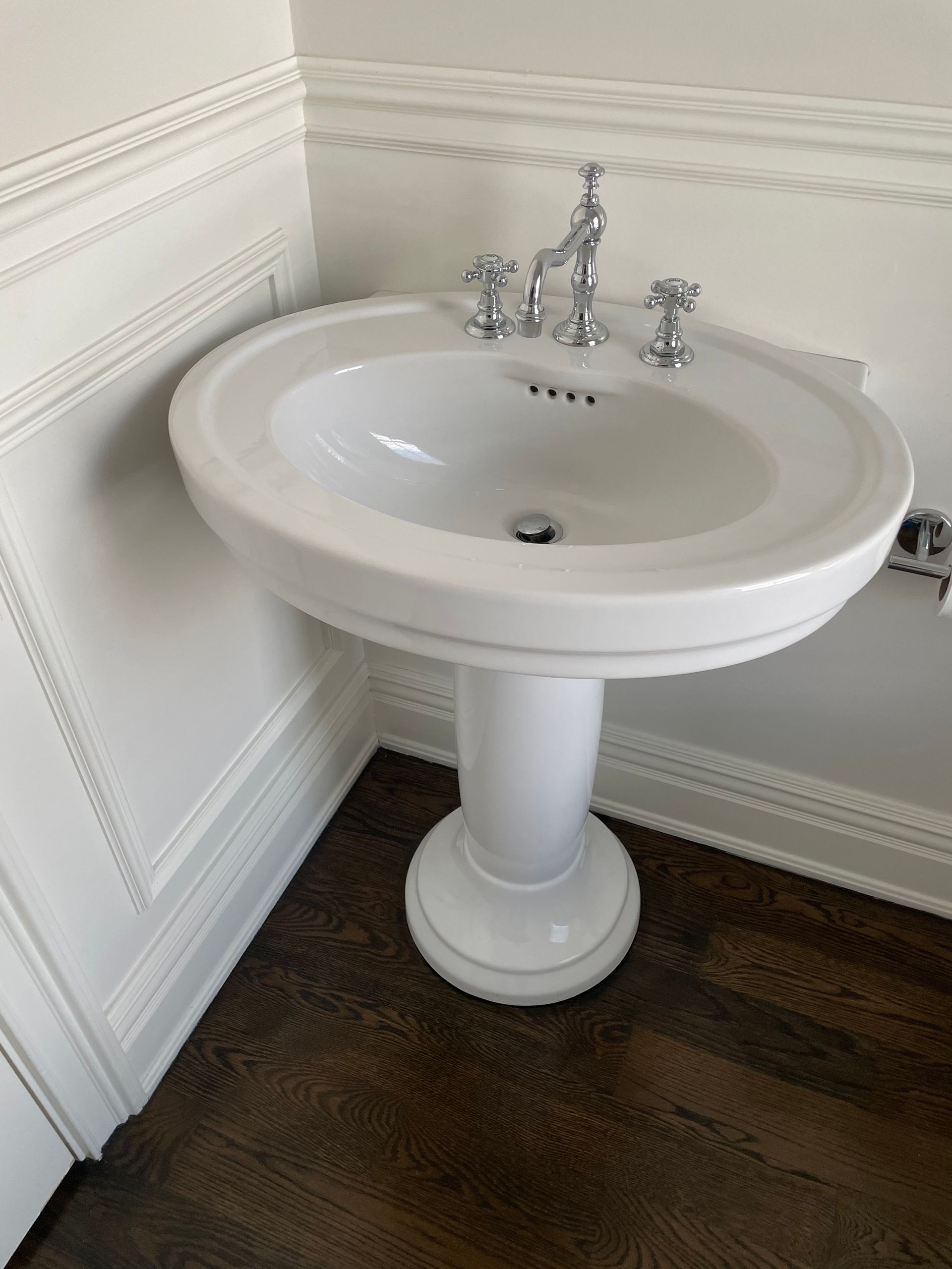 A white pedestal sink in a bathroom with a wooden floor