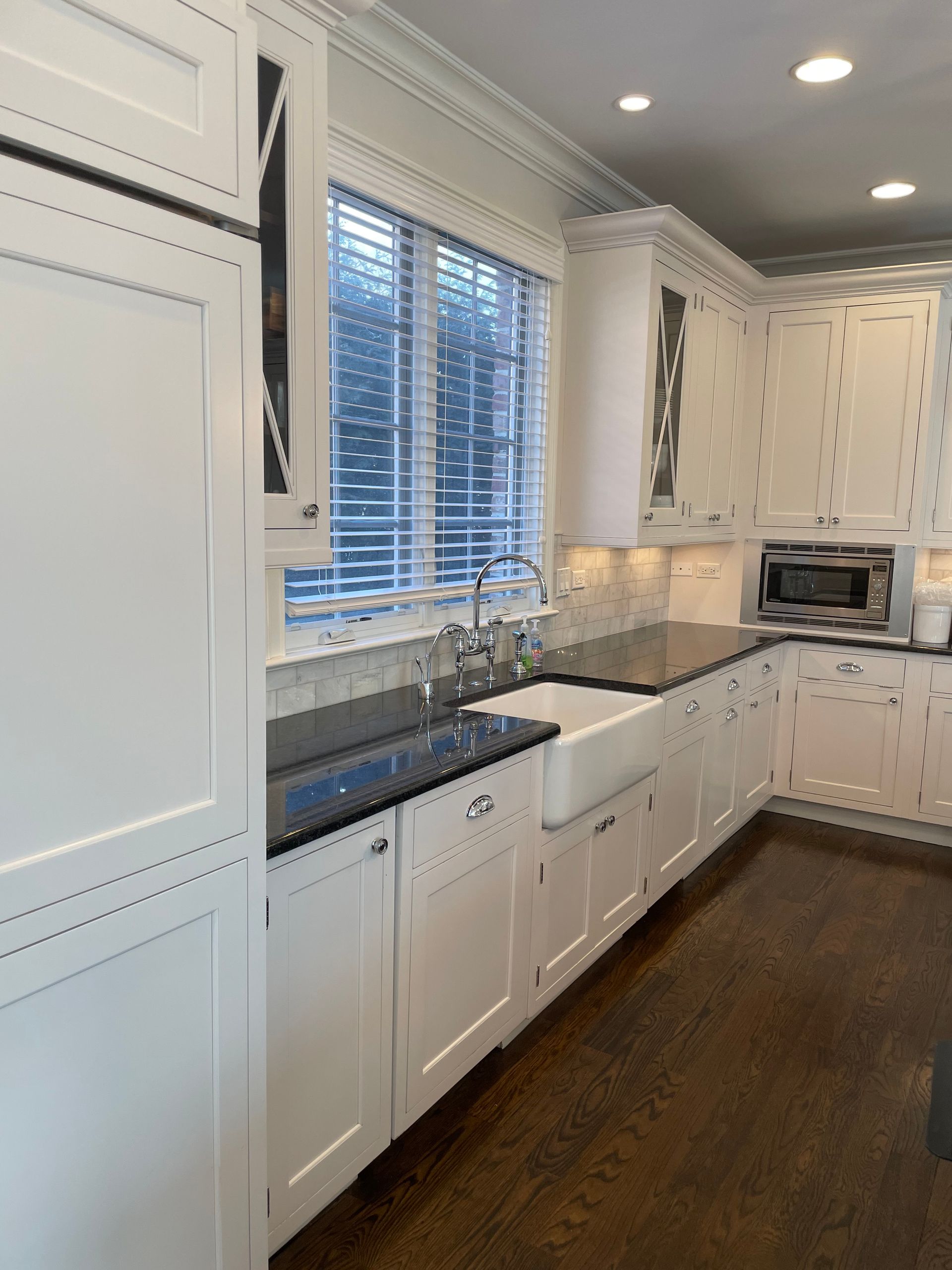 A kitchen with white cabinets , black counter tops , a sink and a window.
