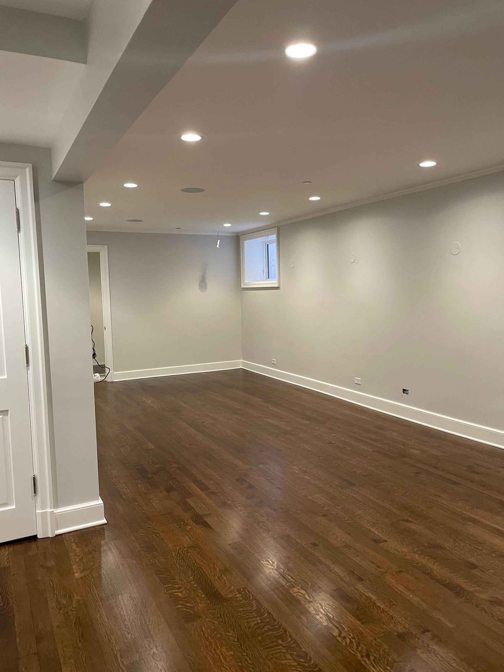 An empty basement with hardwood floors and white walls.