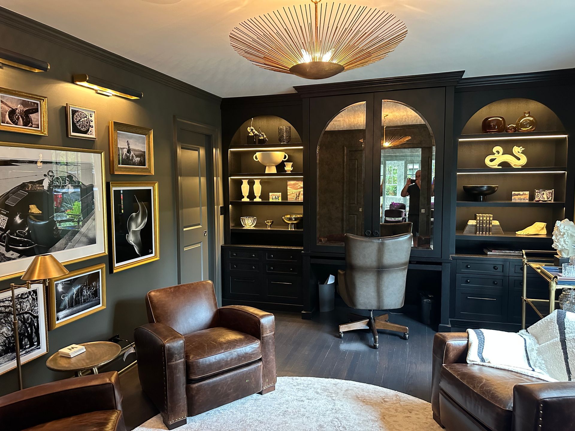 A living room with two leather chairs , a desk and a chandelier.