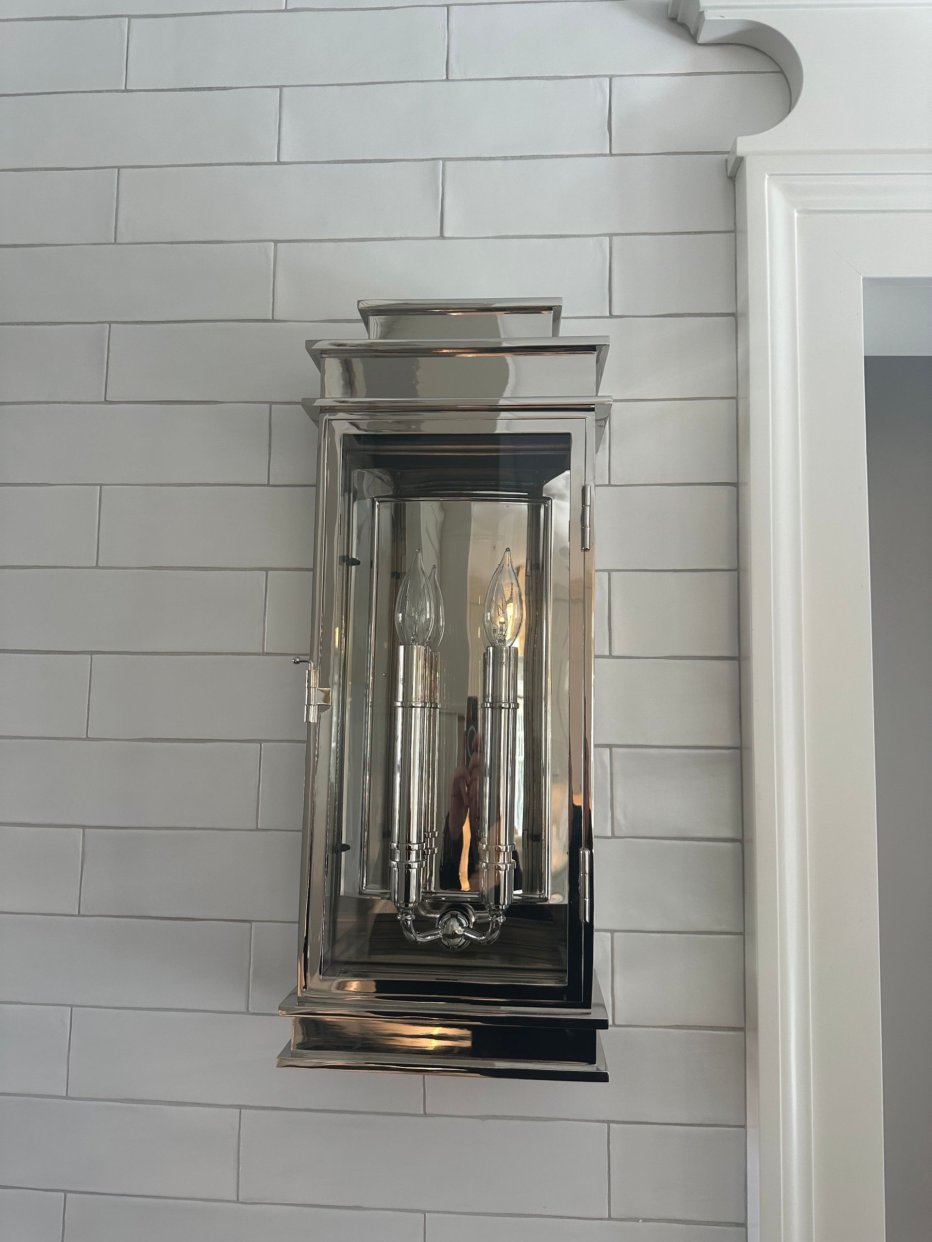 A silver lantern is hanging on a white brick wall.