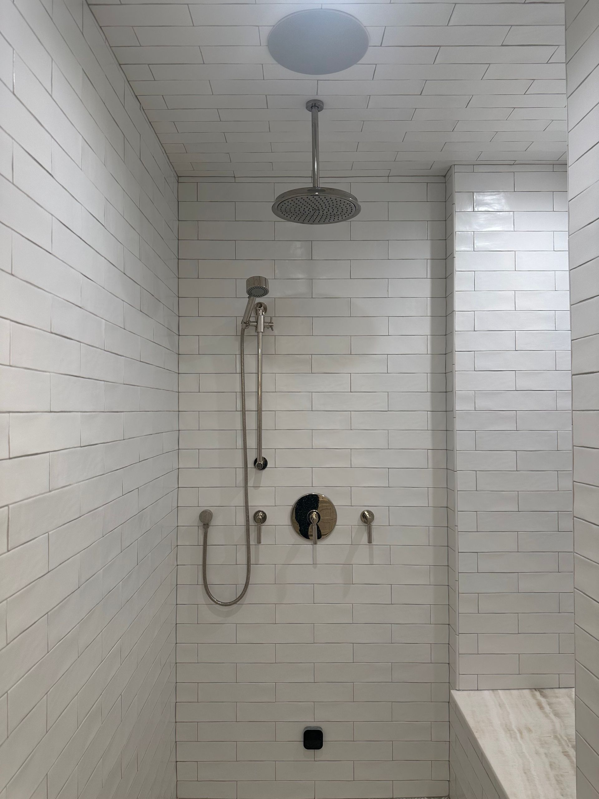 A bathroom with white tiles and a shower head