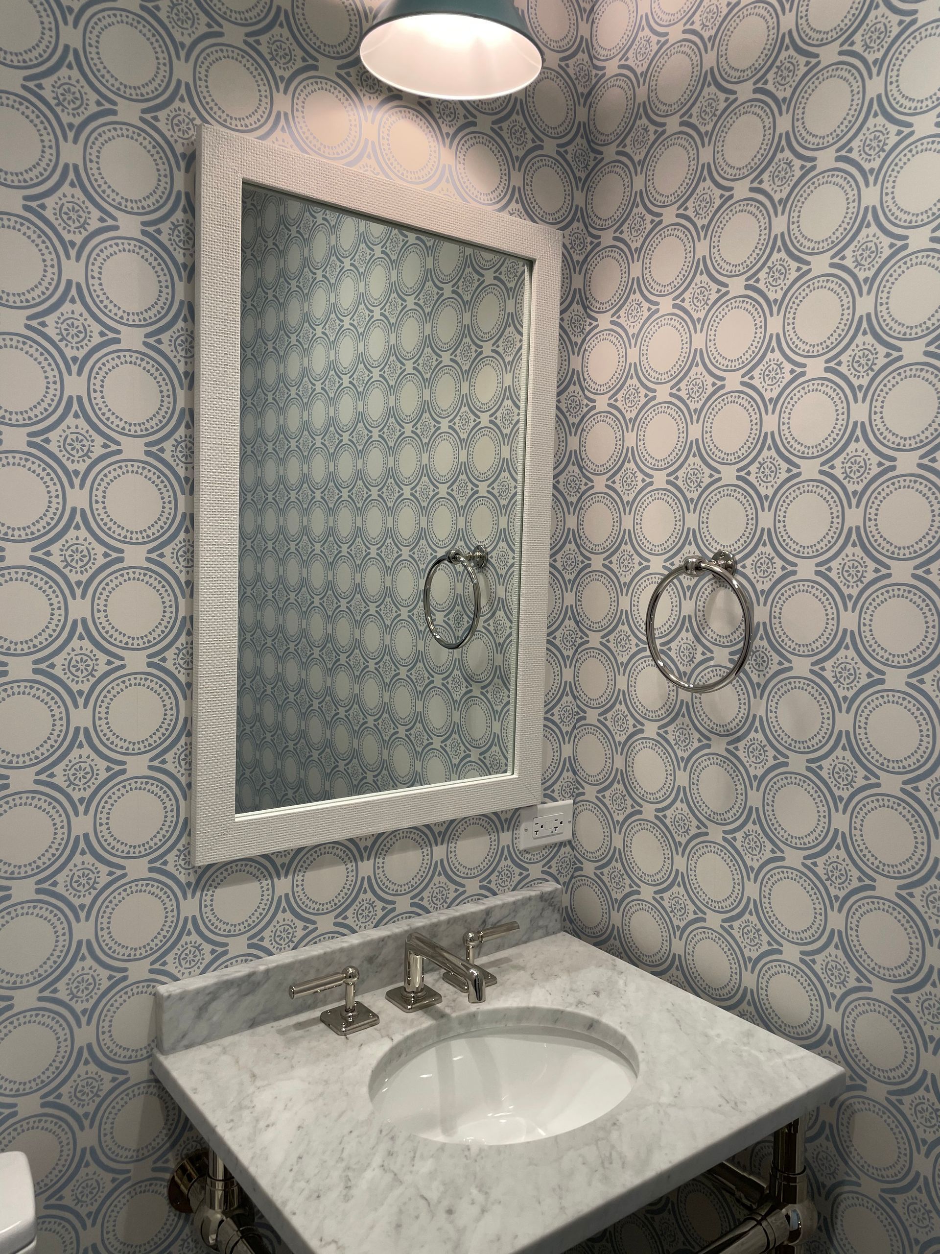 A bathroom with a sink , mirror and wallpaper.
