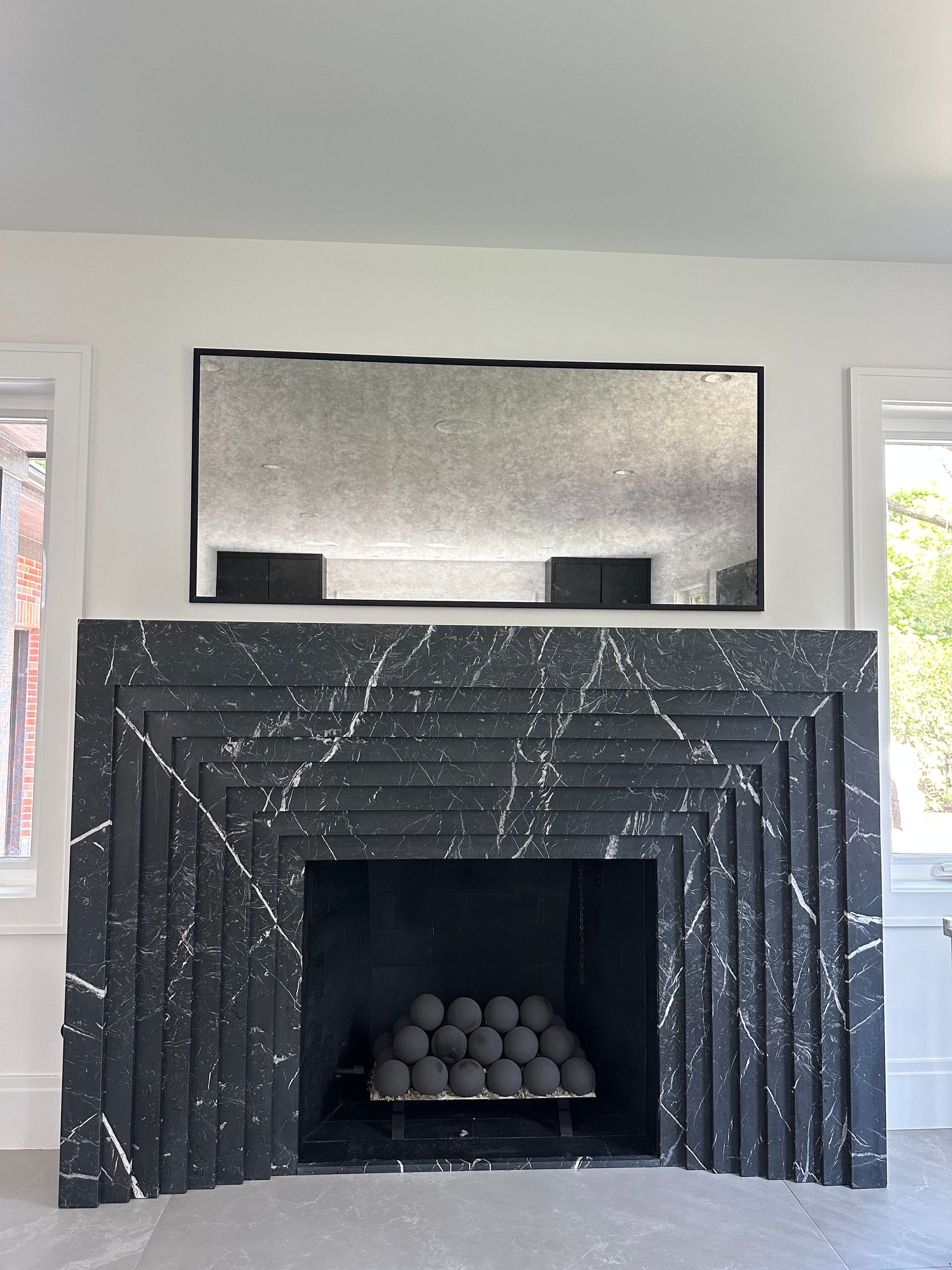 A black fireplace with a mirror above it in a living room.