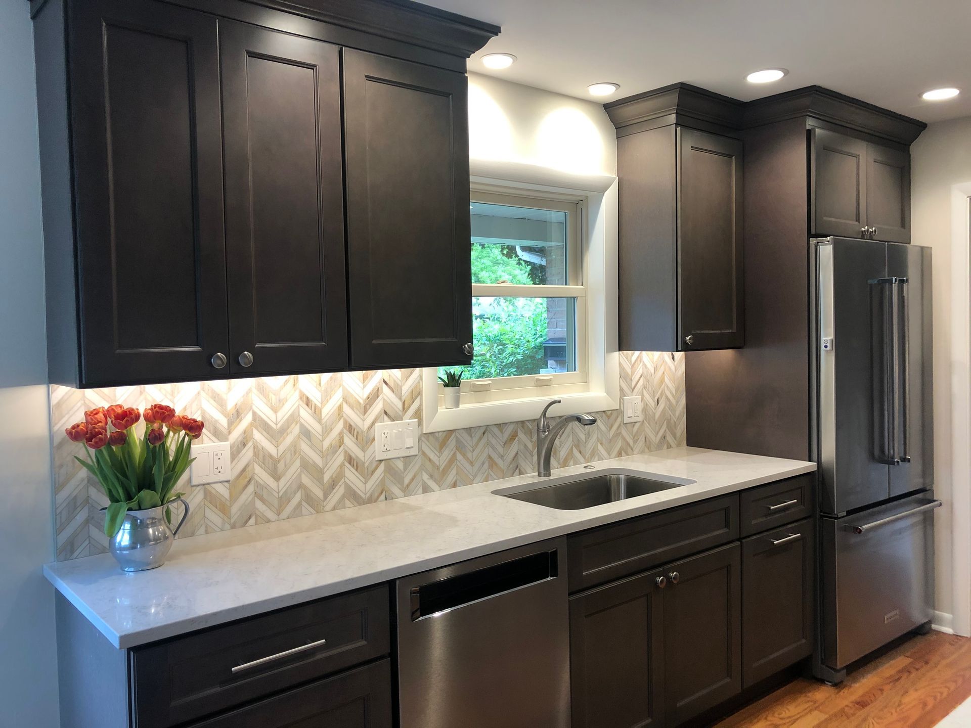 A kitchen with dark cabinets , stainless steel appliances , a sink , and a window.