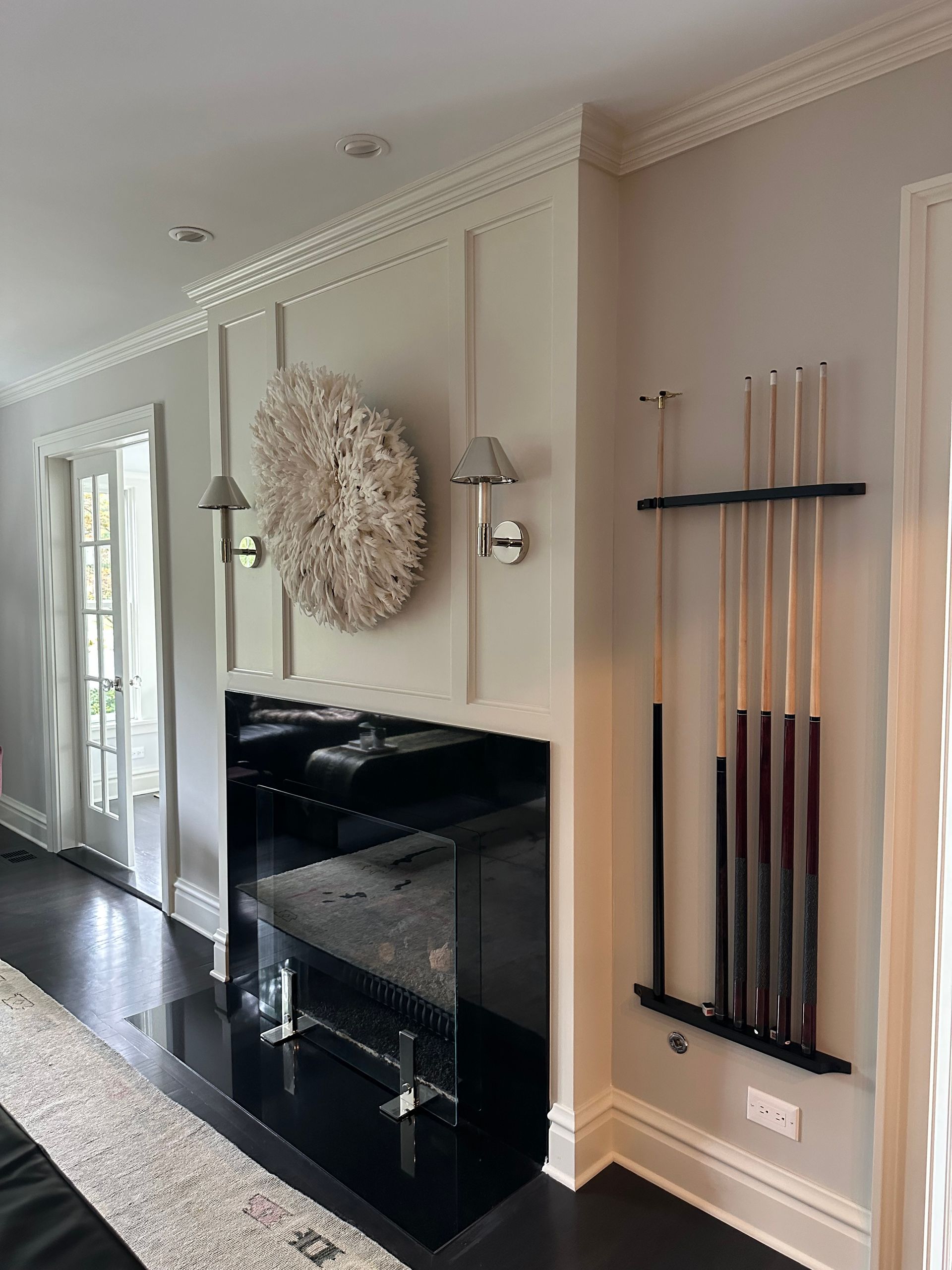 A living room with a fireplace and pool cues hanging on the wall.