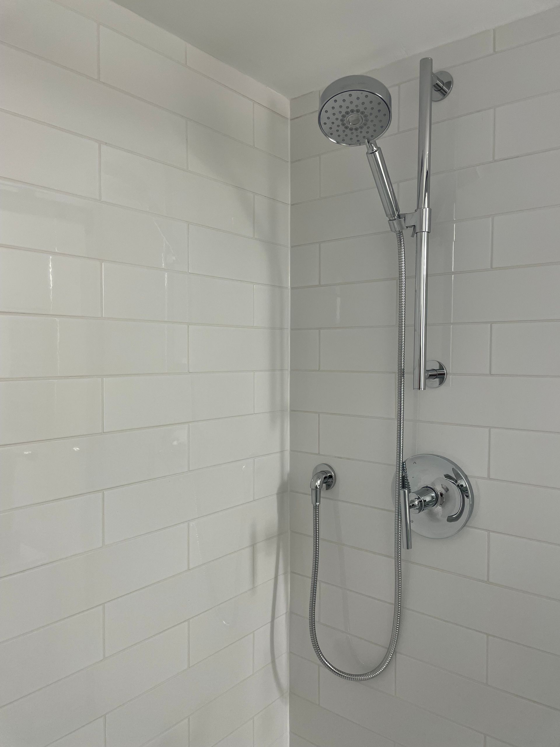A close up of a shower head in a bathroom with white tiles.