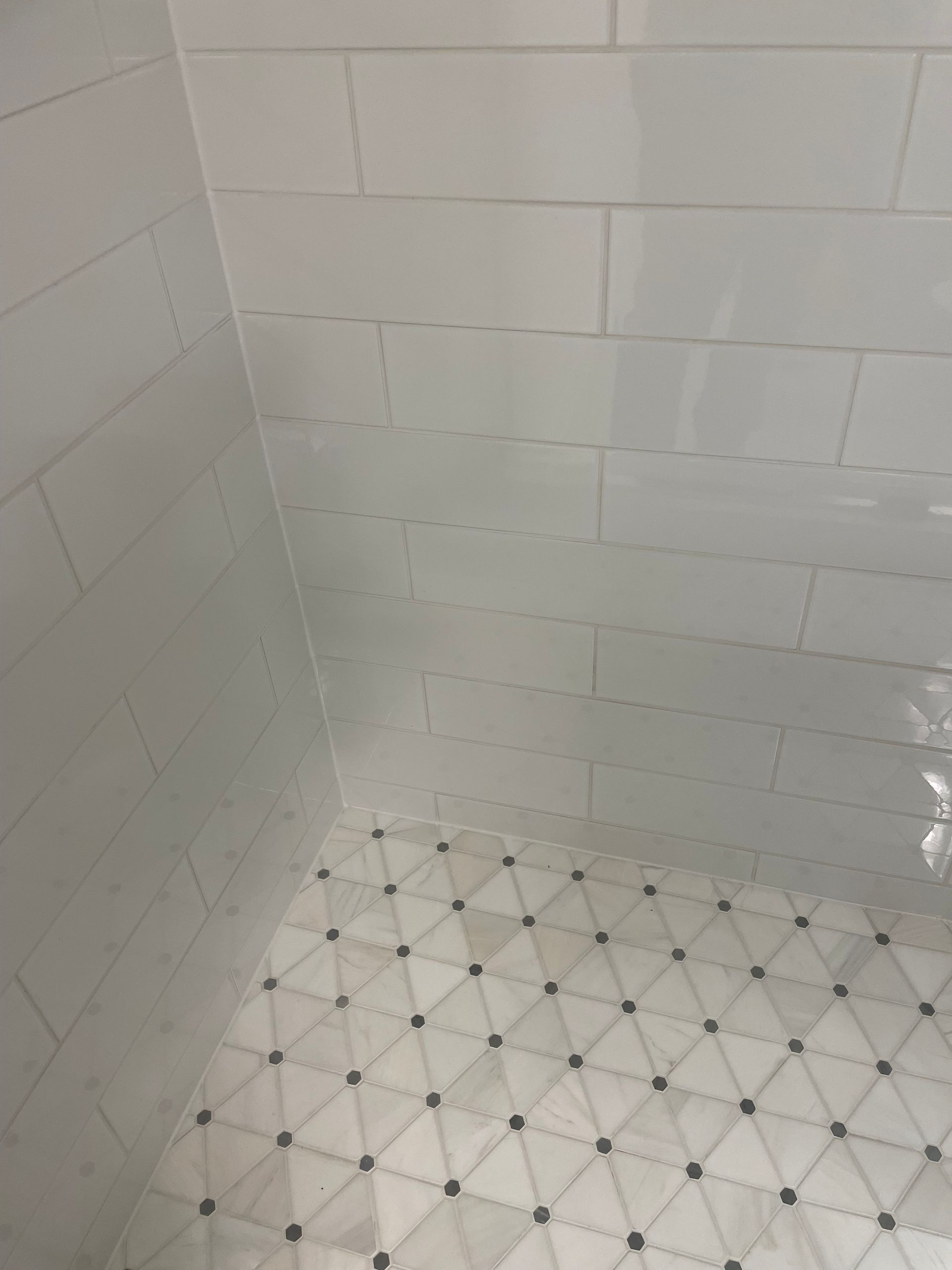 A shower with white tiles and a black and white tile floor.