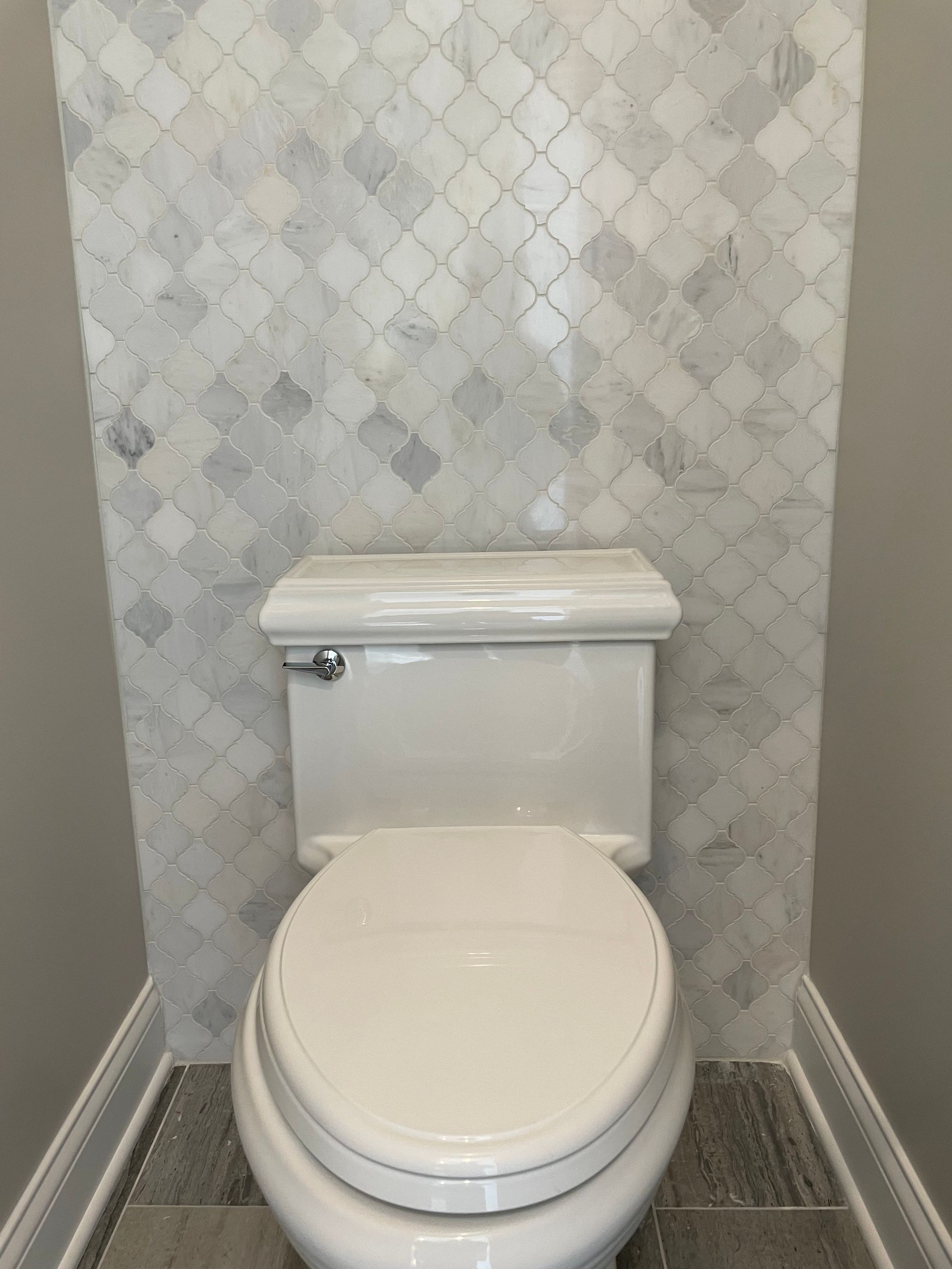 A white toilet is sitting in a bathroom next to a marble wall.