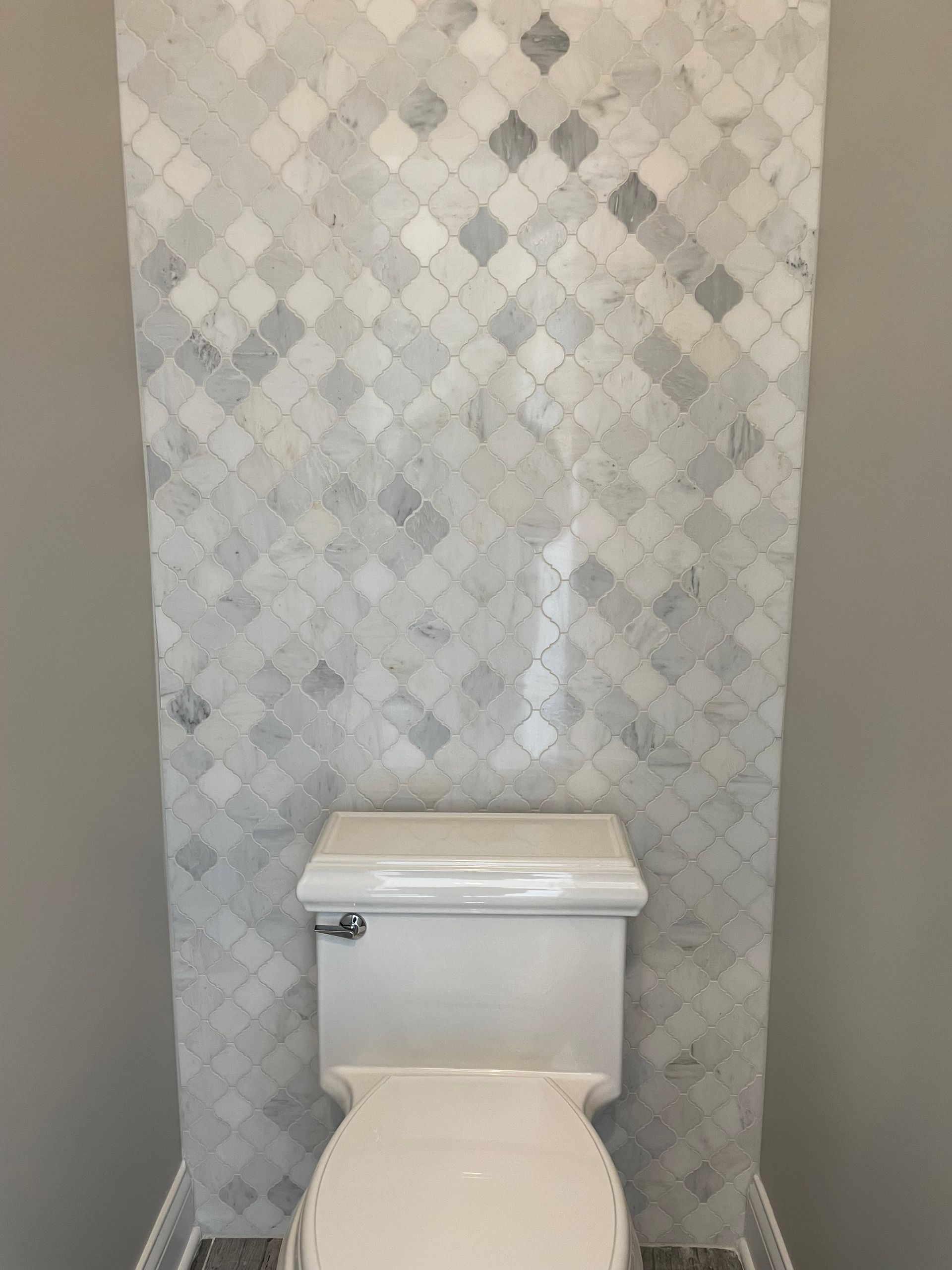 A toilet in a bathroom with a marble wall behind it.