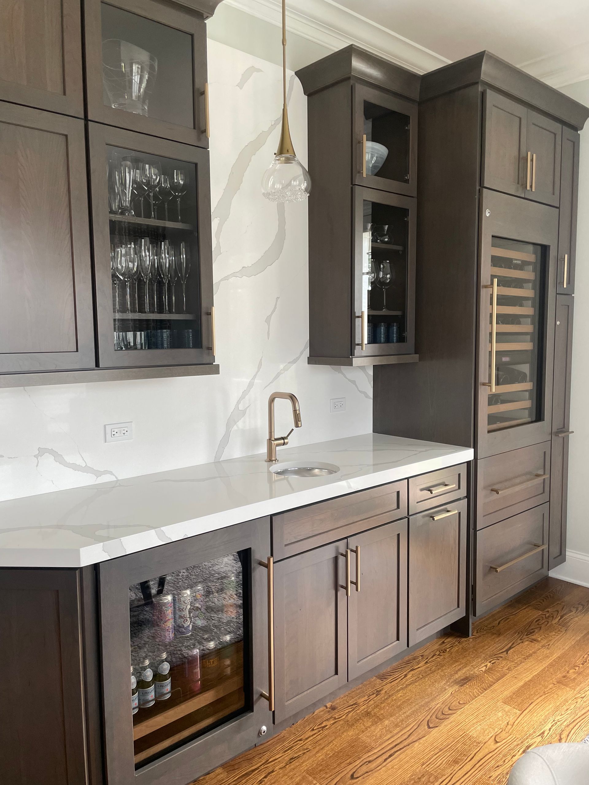 A kitchen with wooden cabinets , a sink , a refrigerator and a wine cooler.