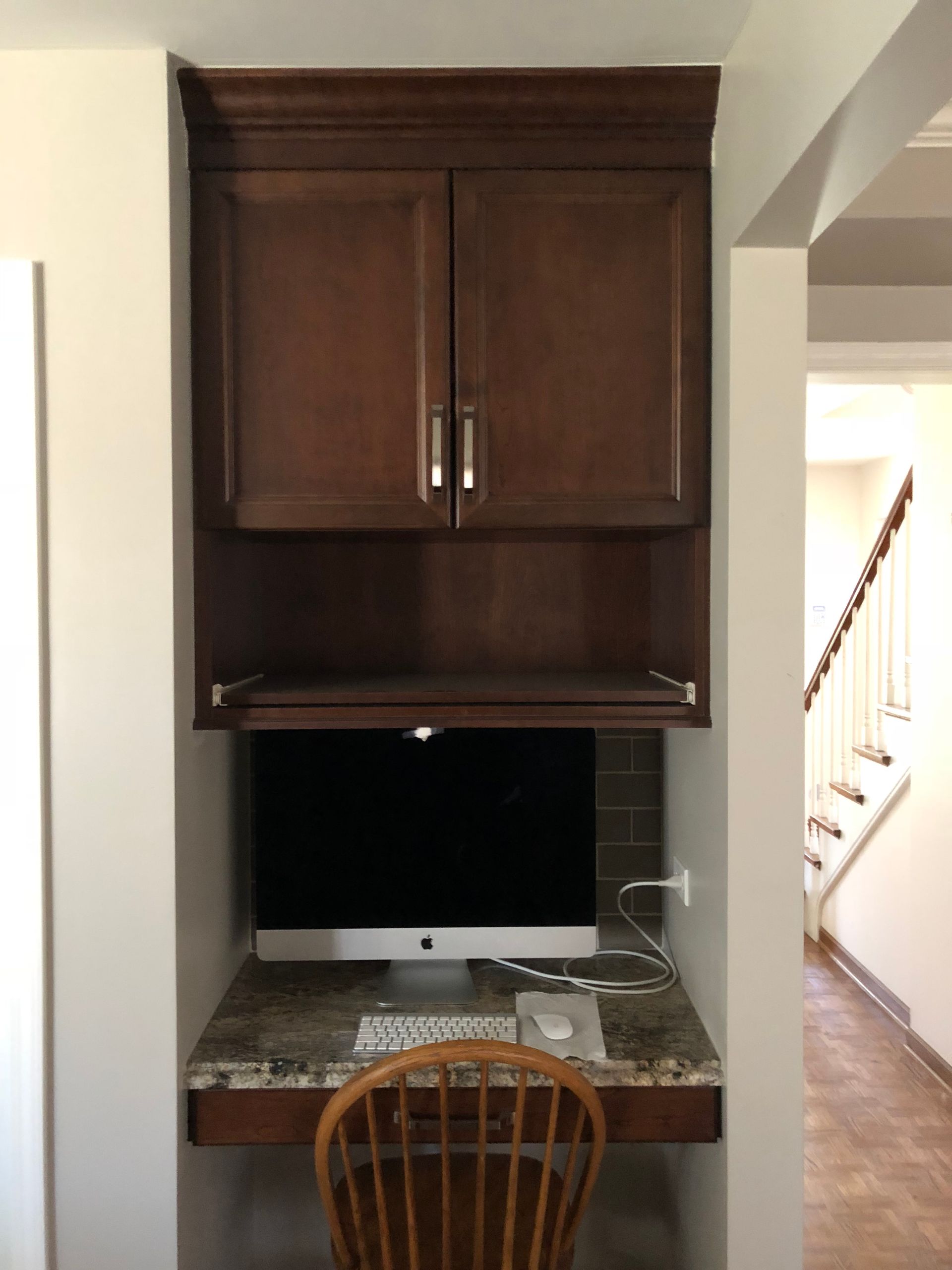 A computer sits on a desk under a cabinet