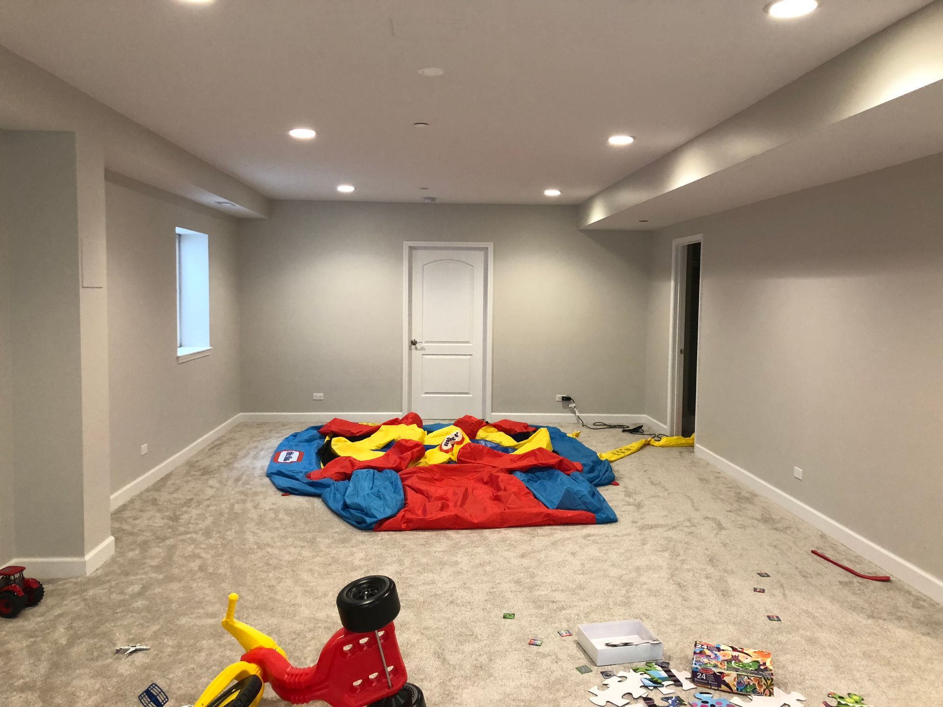 An empty basement with a bouncy house and toys on the floor.