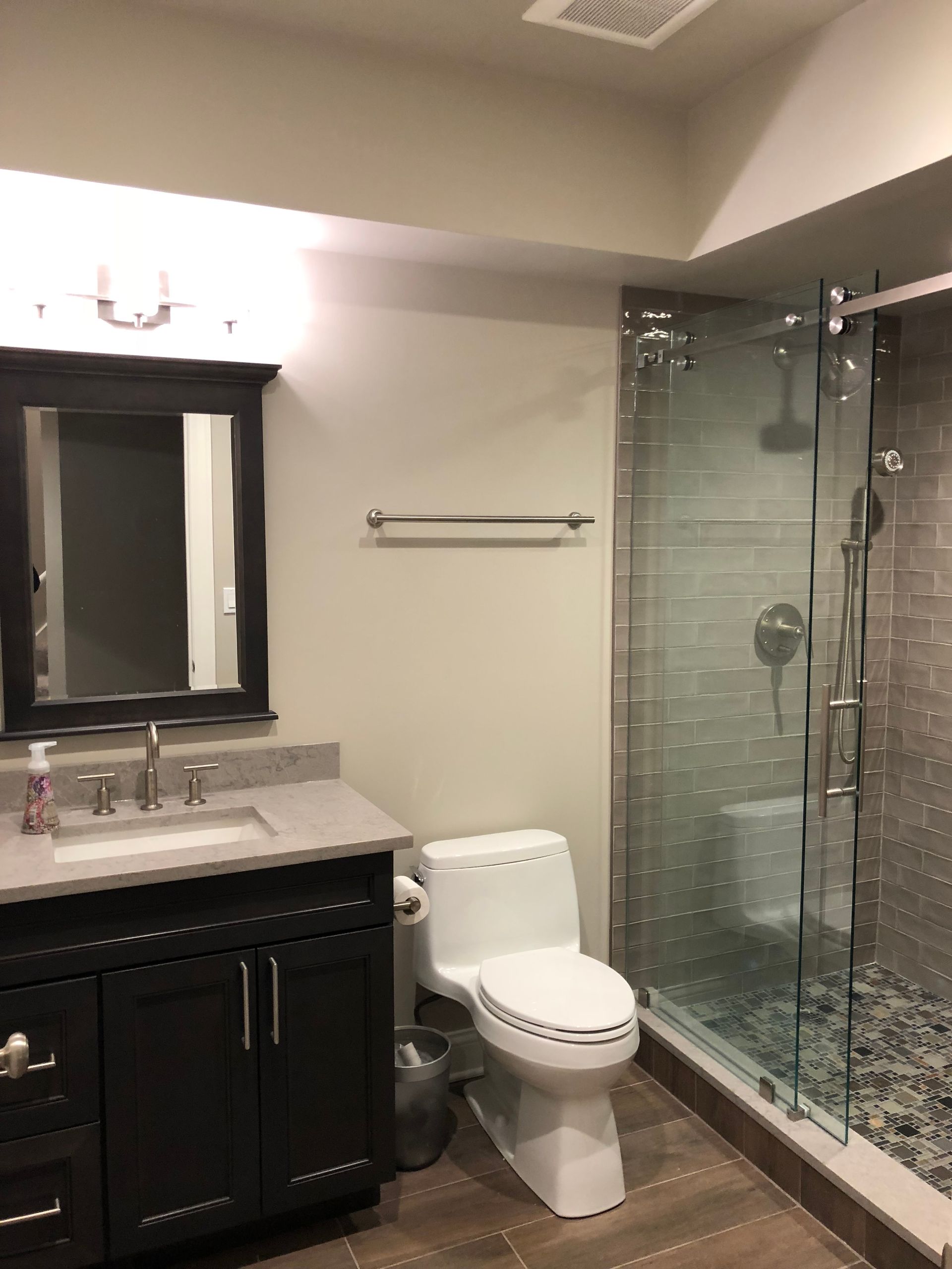 A bathroom with a toilet , sink , mirror and walk in shower.