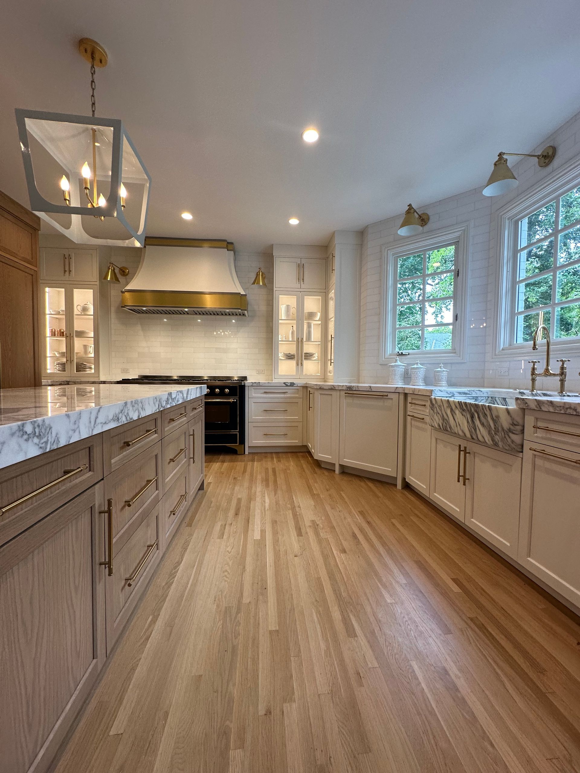 A kitchen with hardwood floors , white cabinets , marble counter tops and a stove.