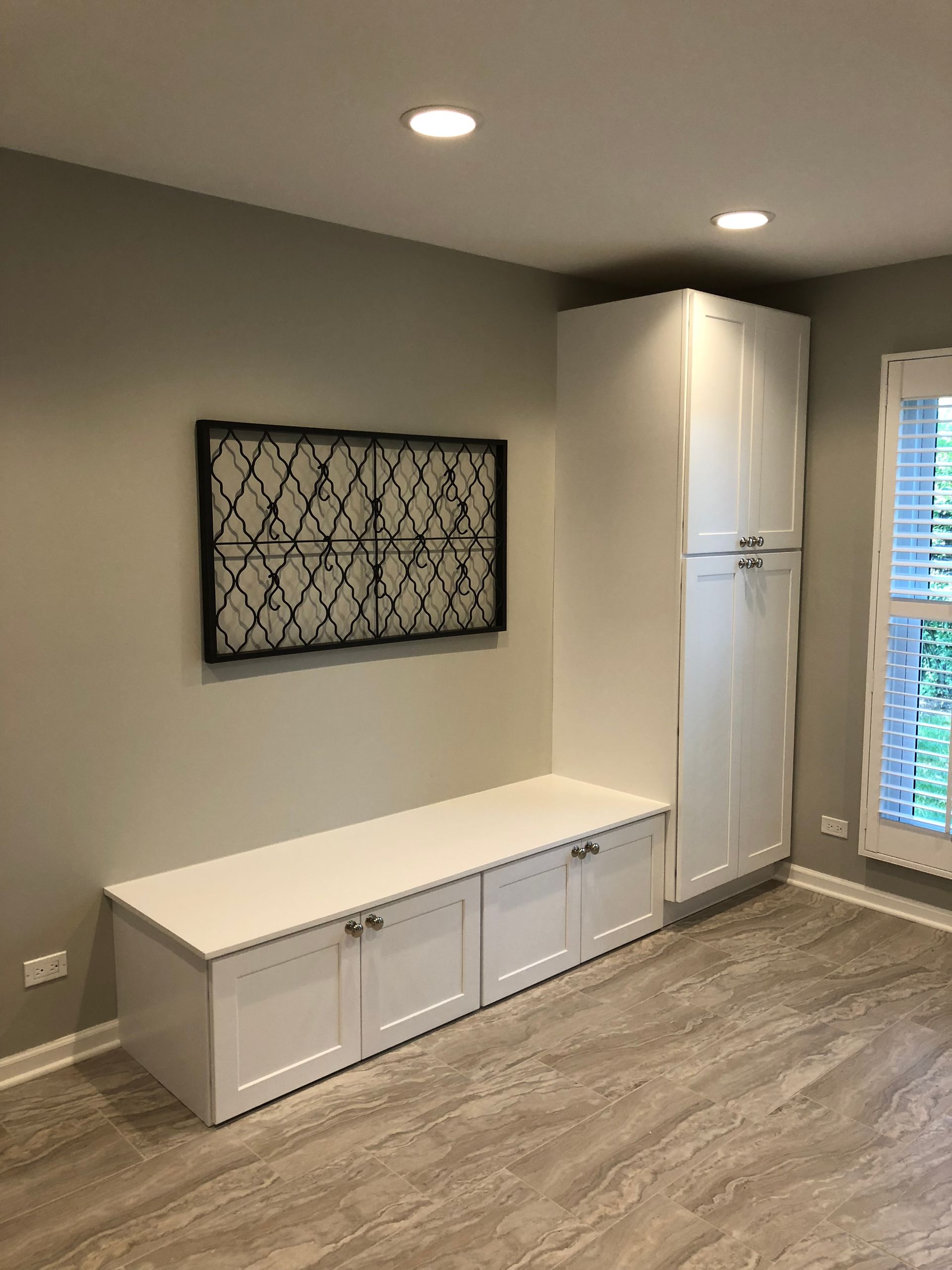 A room with a bench , cabinets , and a window.
