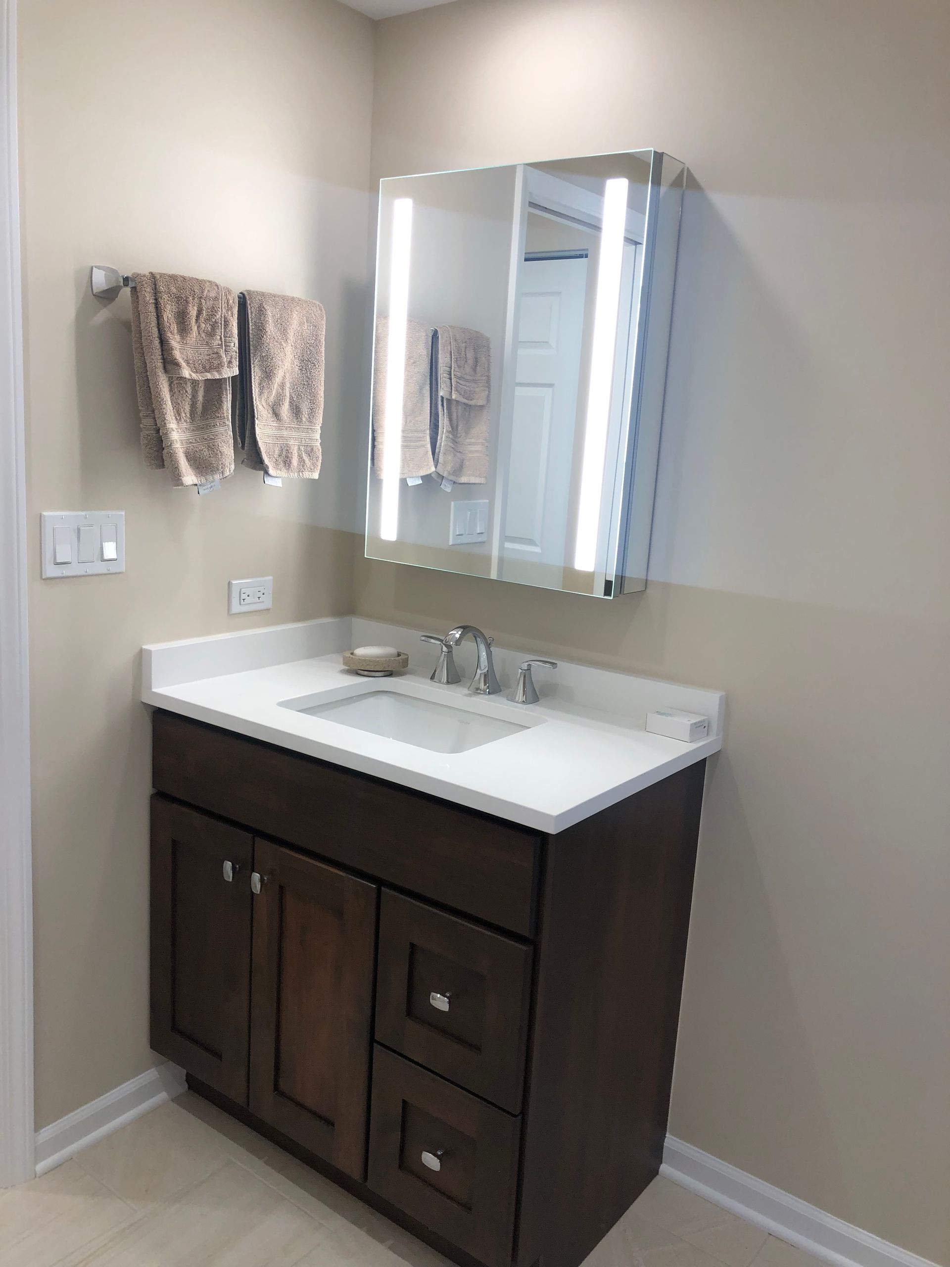 A bathroom with a sink , mirror and towels hanging on the wall.