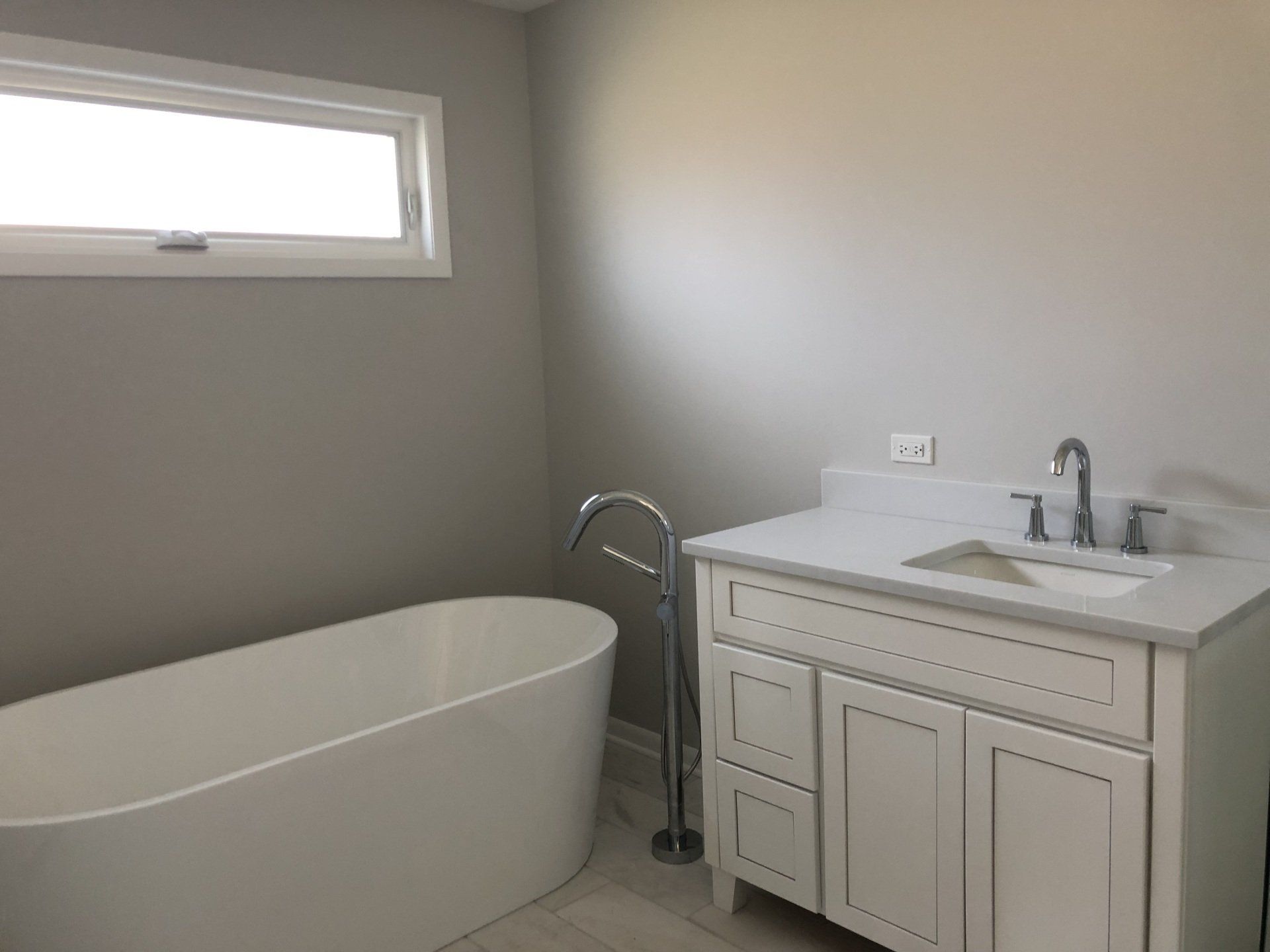 A bathroom with a tub , sink , and window.