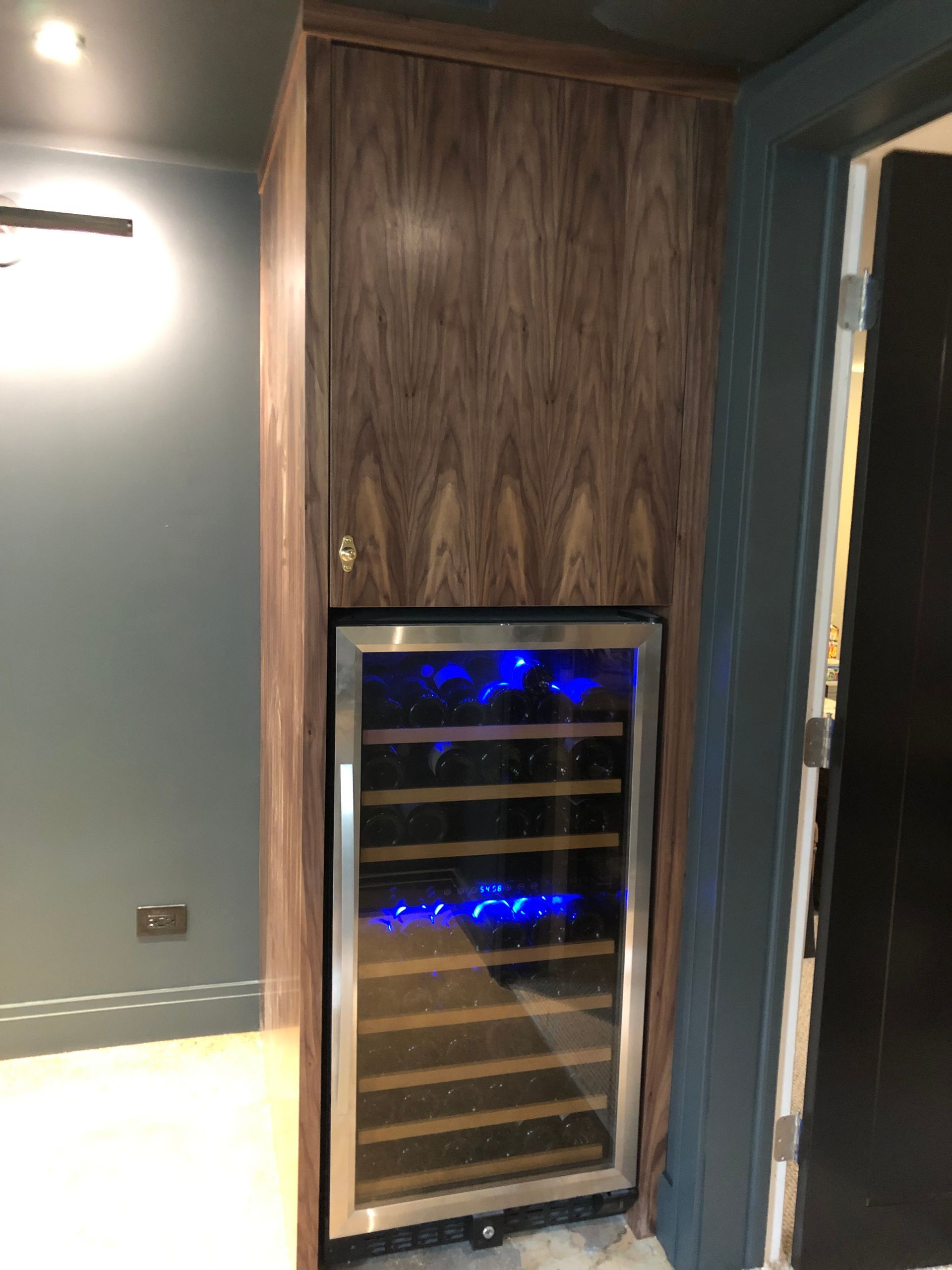 A wine cooler is built into a wooden cabinet in a room.