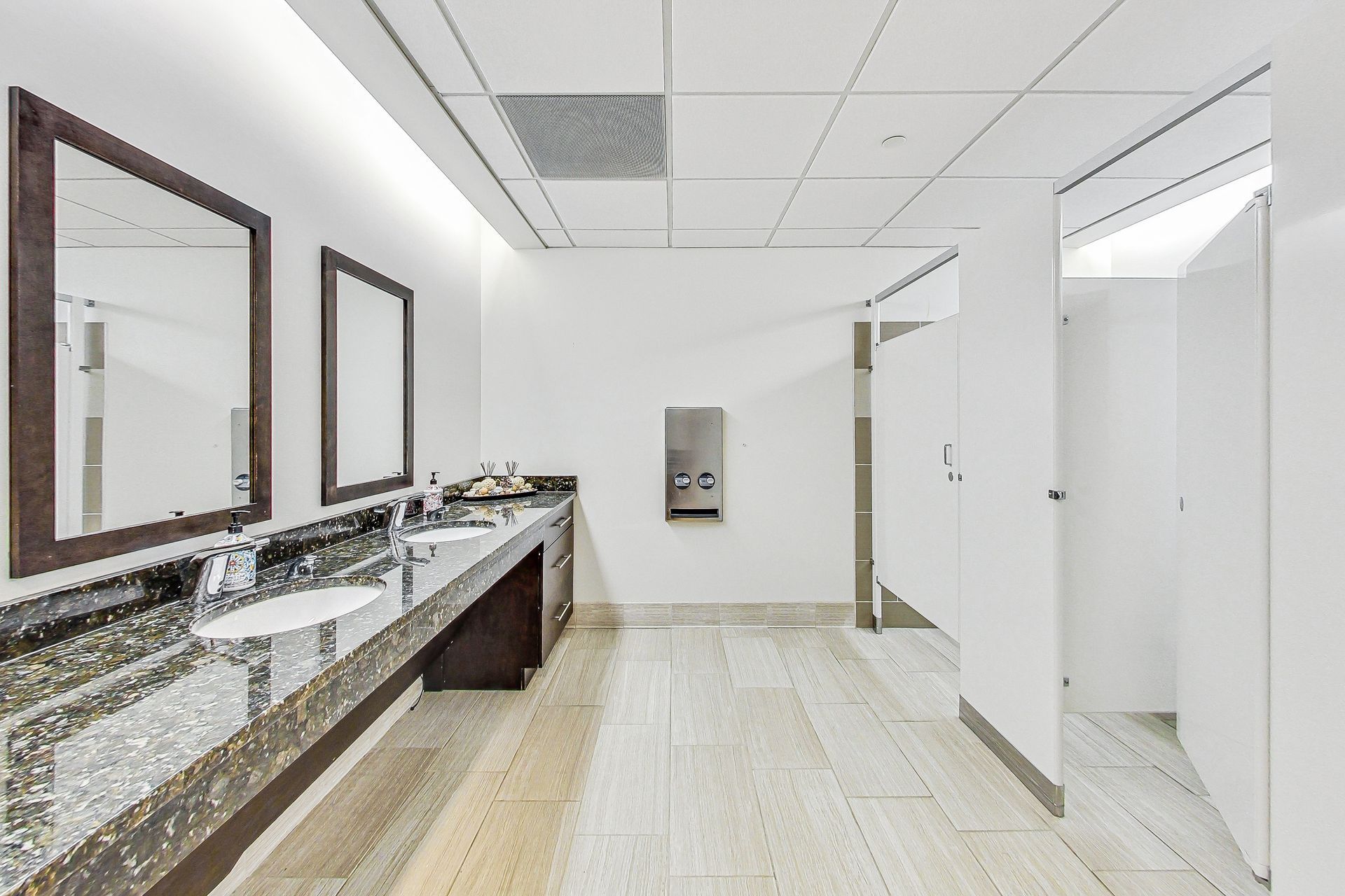 A bathroom with two sinks , two mirrors and a toilet.