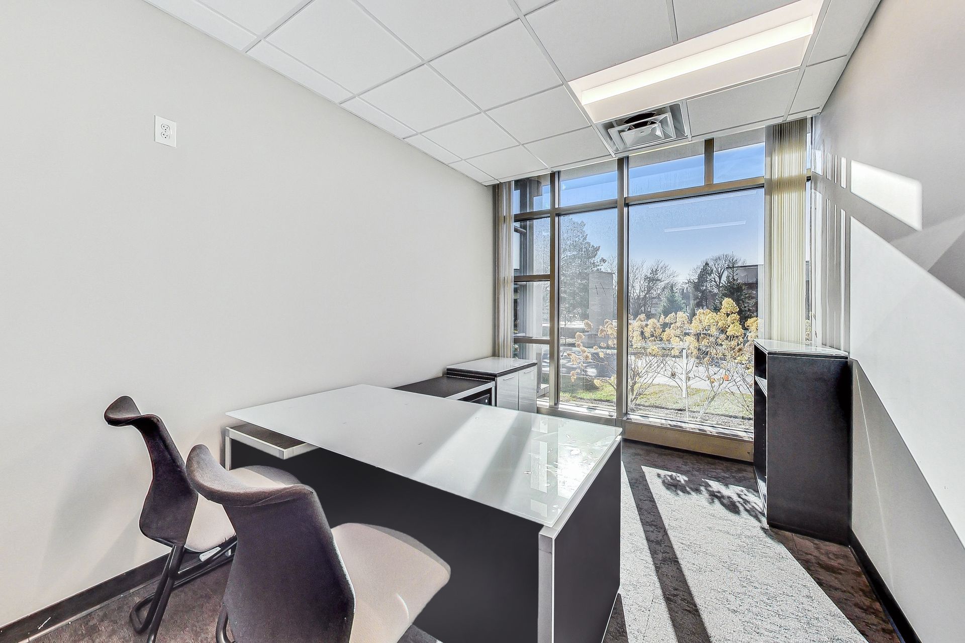 A small office with a desk and chairs and a large window.