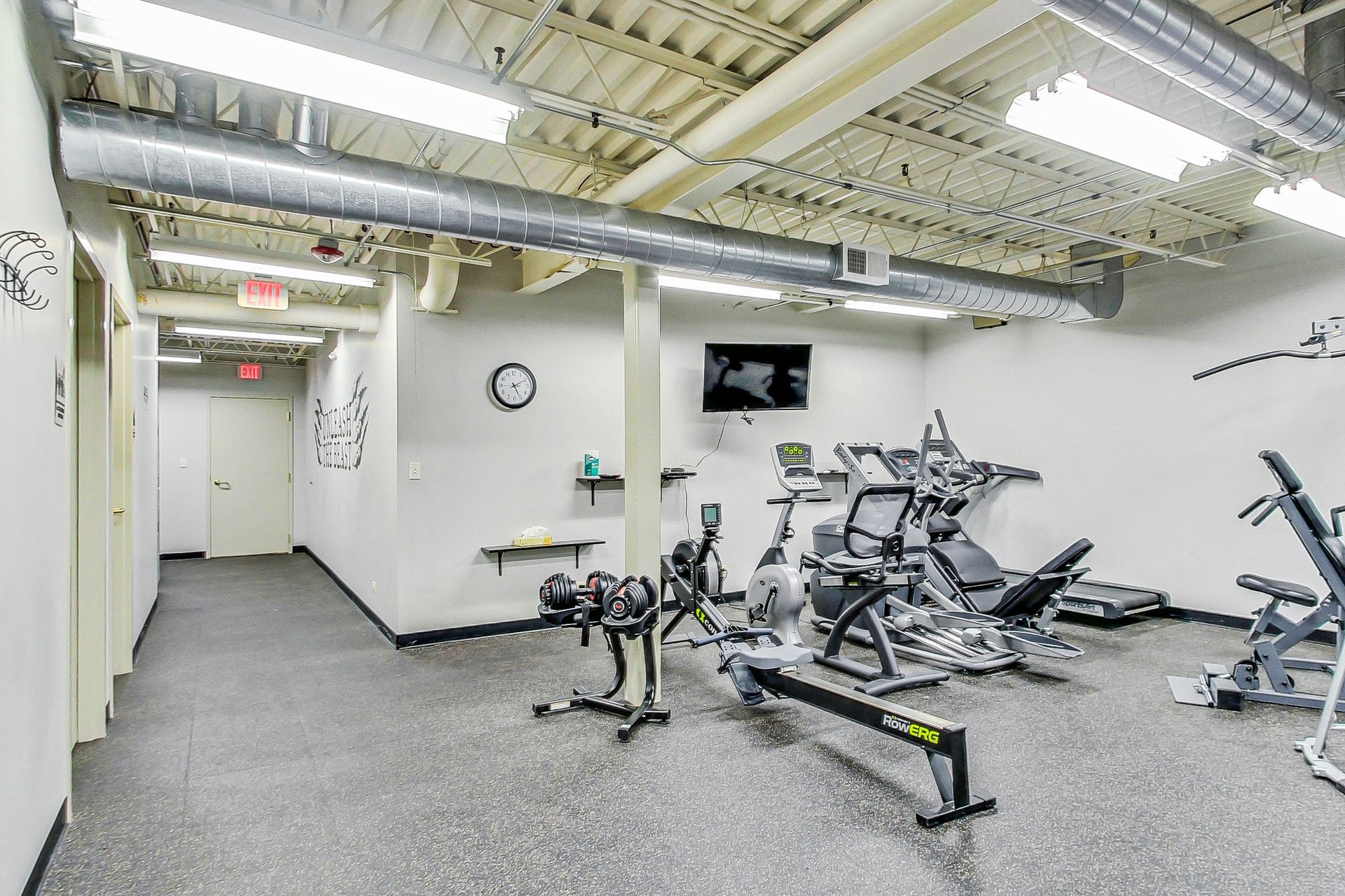 A gym with a lot of exercise equipment and a clock on the wall.