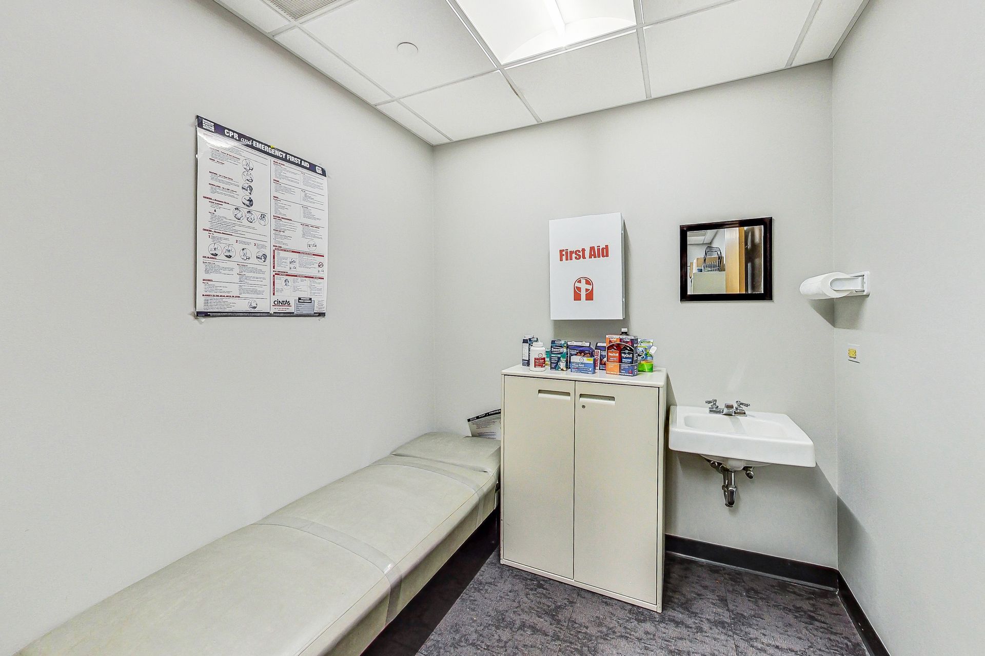 A doctor 's office with a bed , sink and mirror.