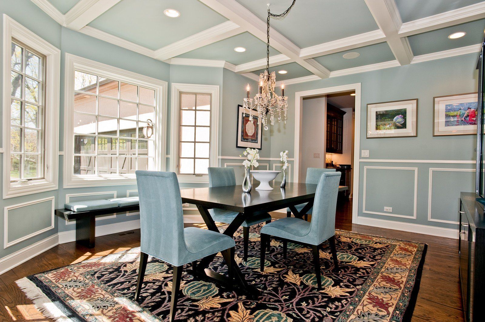 Dining room with blue walls, chandelier, dark table, and patterned rug.